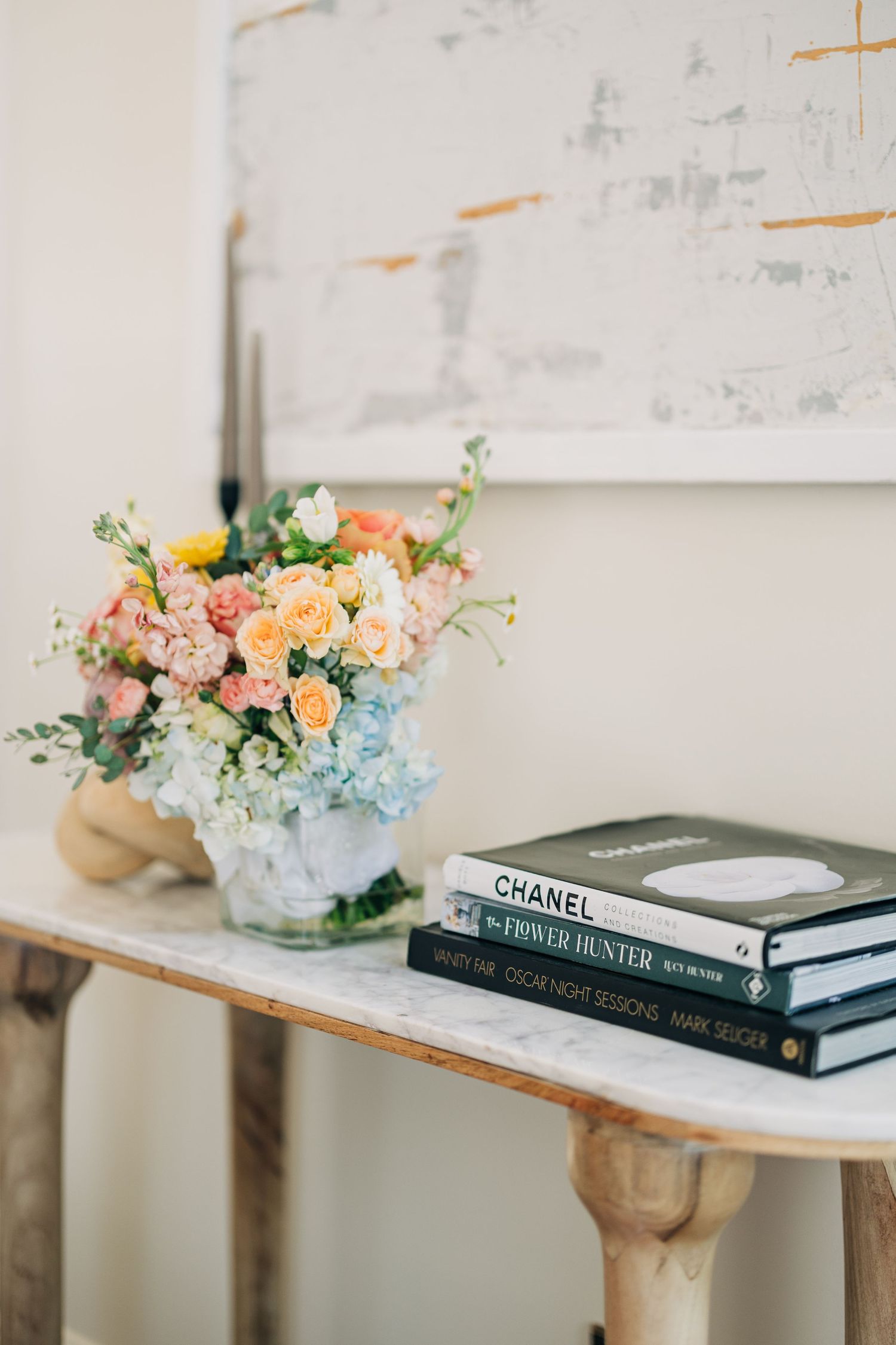 Marble console table styled with pastel floral arrangement and stacked Chanel, Flower Hunter, and Oscar Night Sessions coffee table books.