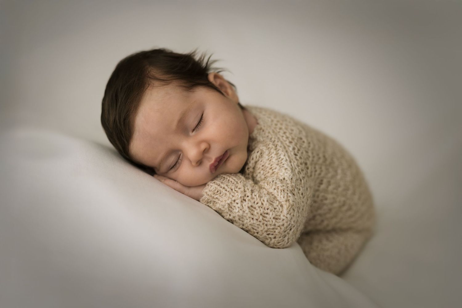 A sleeping figure rests peacefully on white bedding while wearing a cozy beige knit sweater.