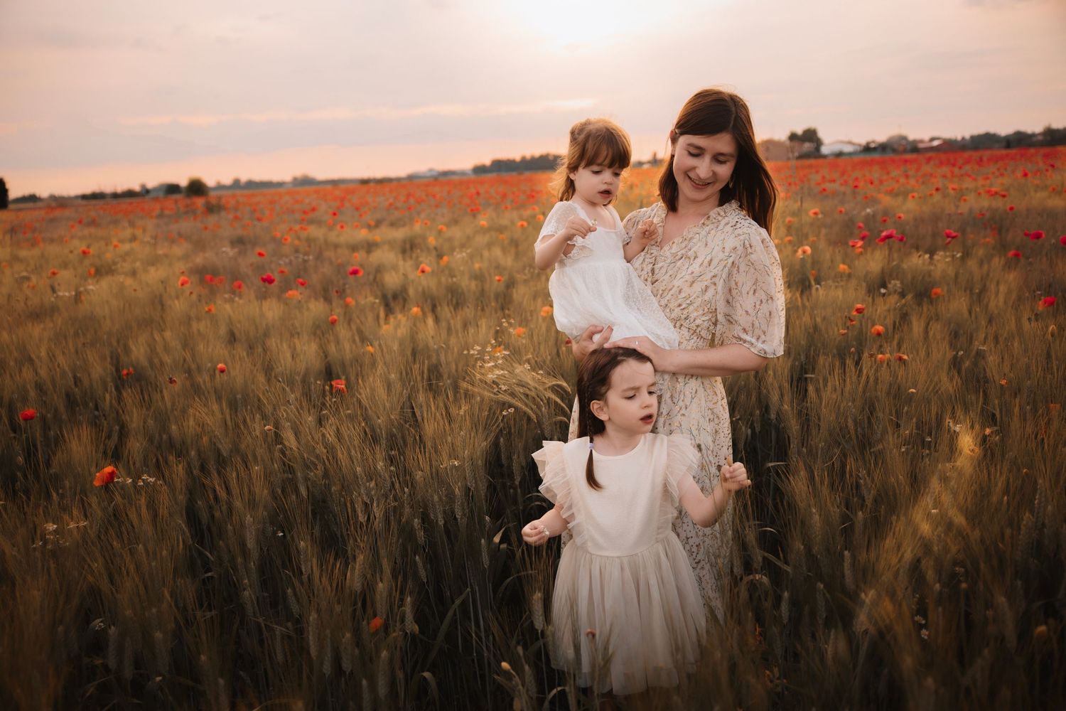 A family stands together in a golden wheat field with red poppies during sunset.