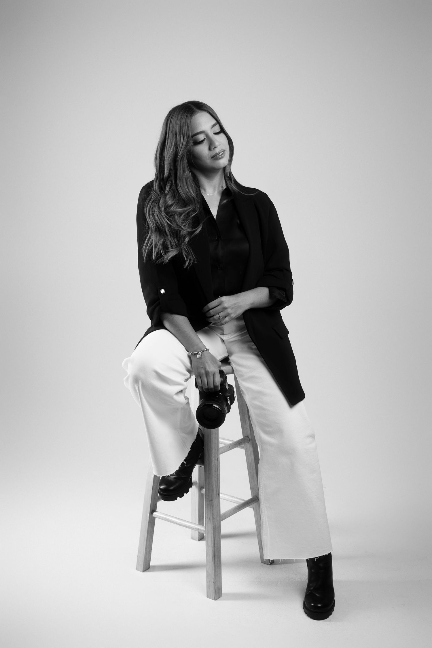 Artistic black and white photo of a photographer posing with camera on wooden stool.