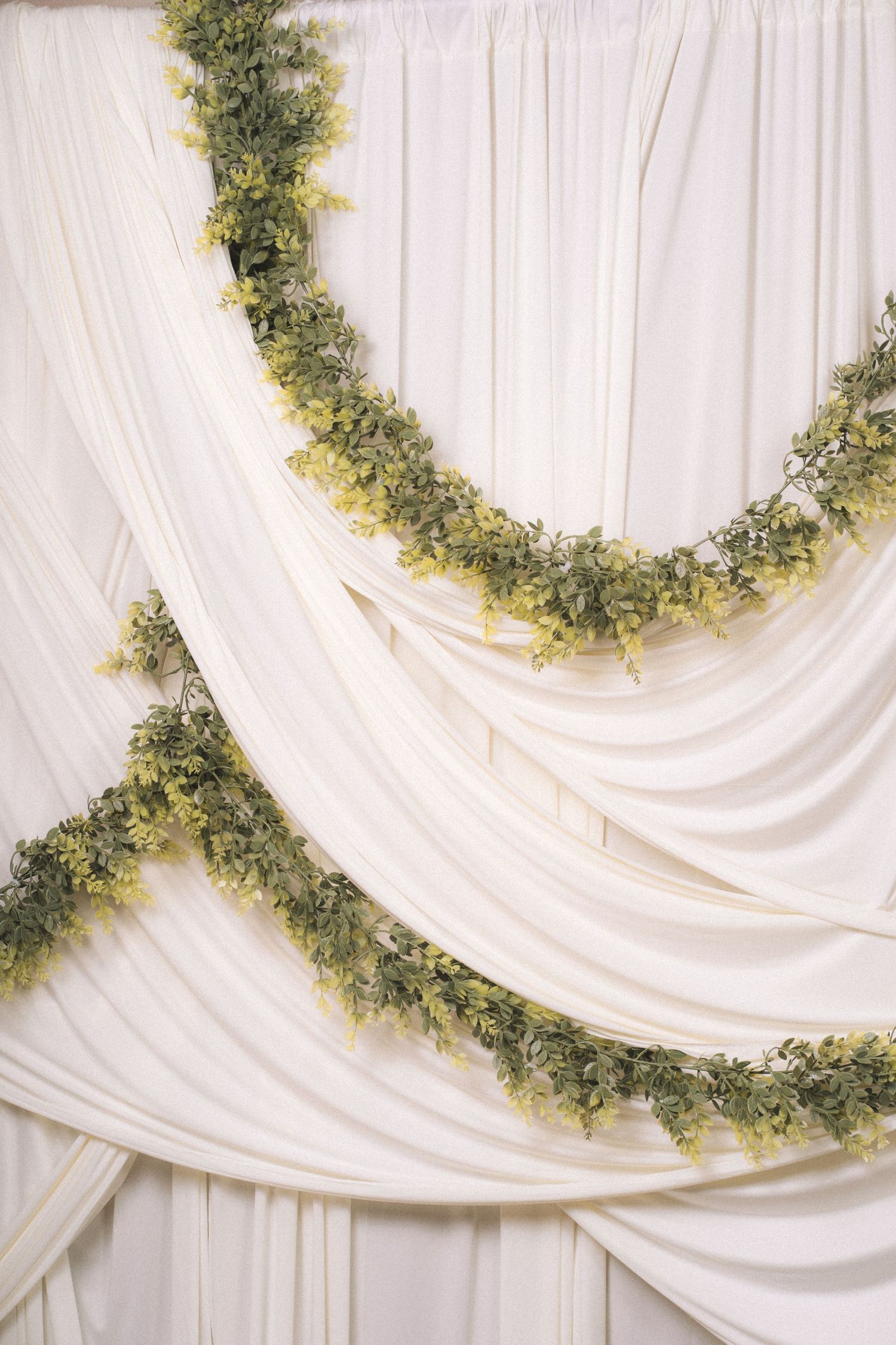 Elegant white draped fabric backdrop decorated with lush green garland swags for a wedding ceremony.