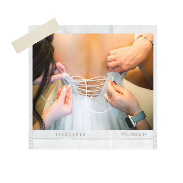 Hands lacing up the back of a white wedding dress on a bride, captured in a vintage Polaroid-style photo.