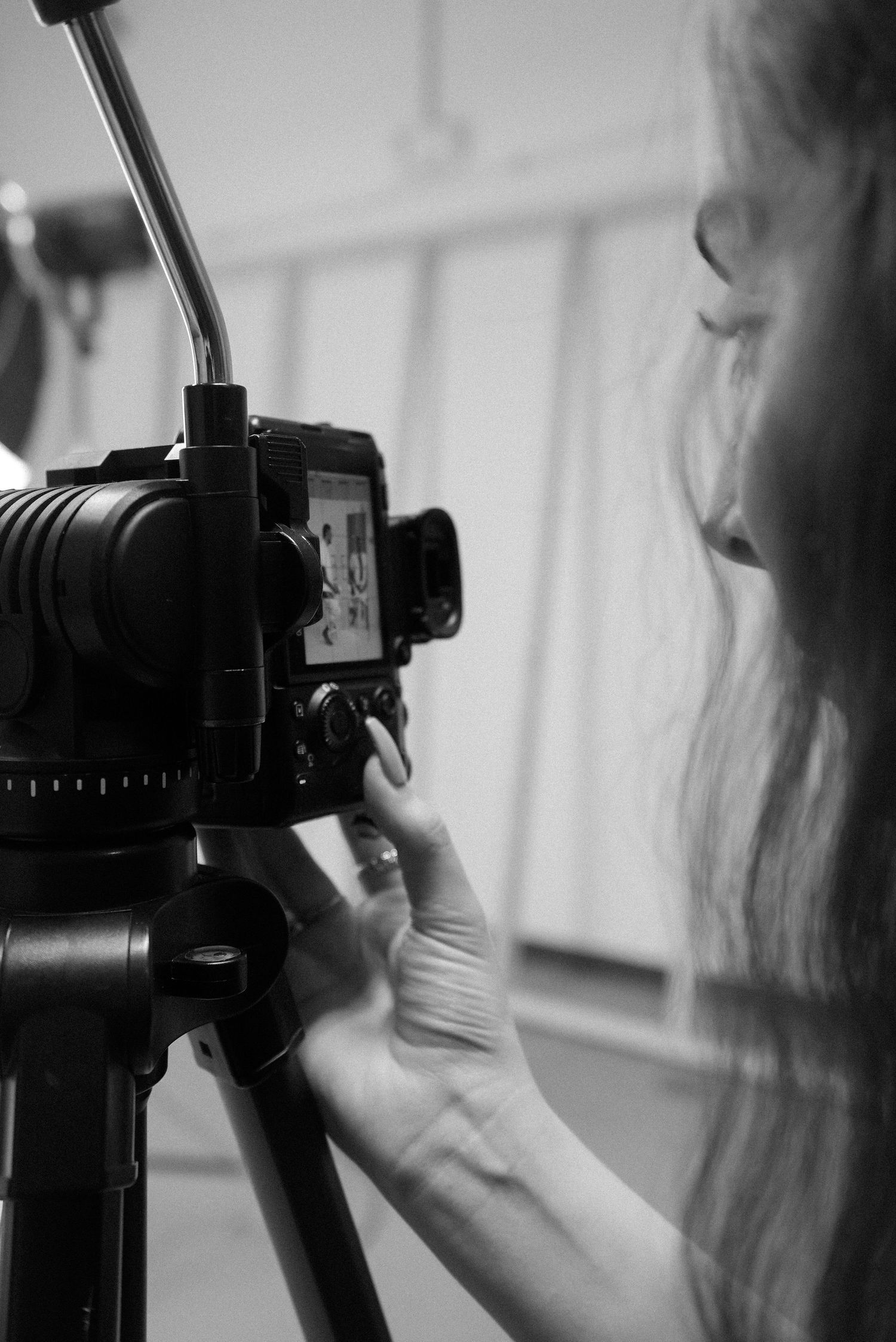 Black and white close-up of a photographer (Ellie) adjusting camera settings on a tripod.