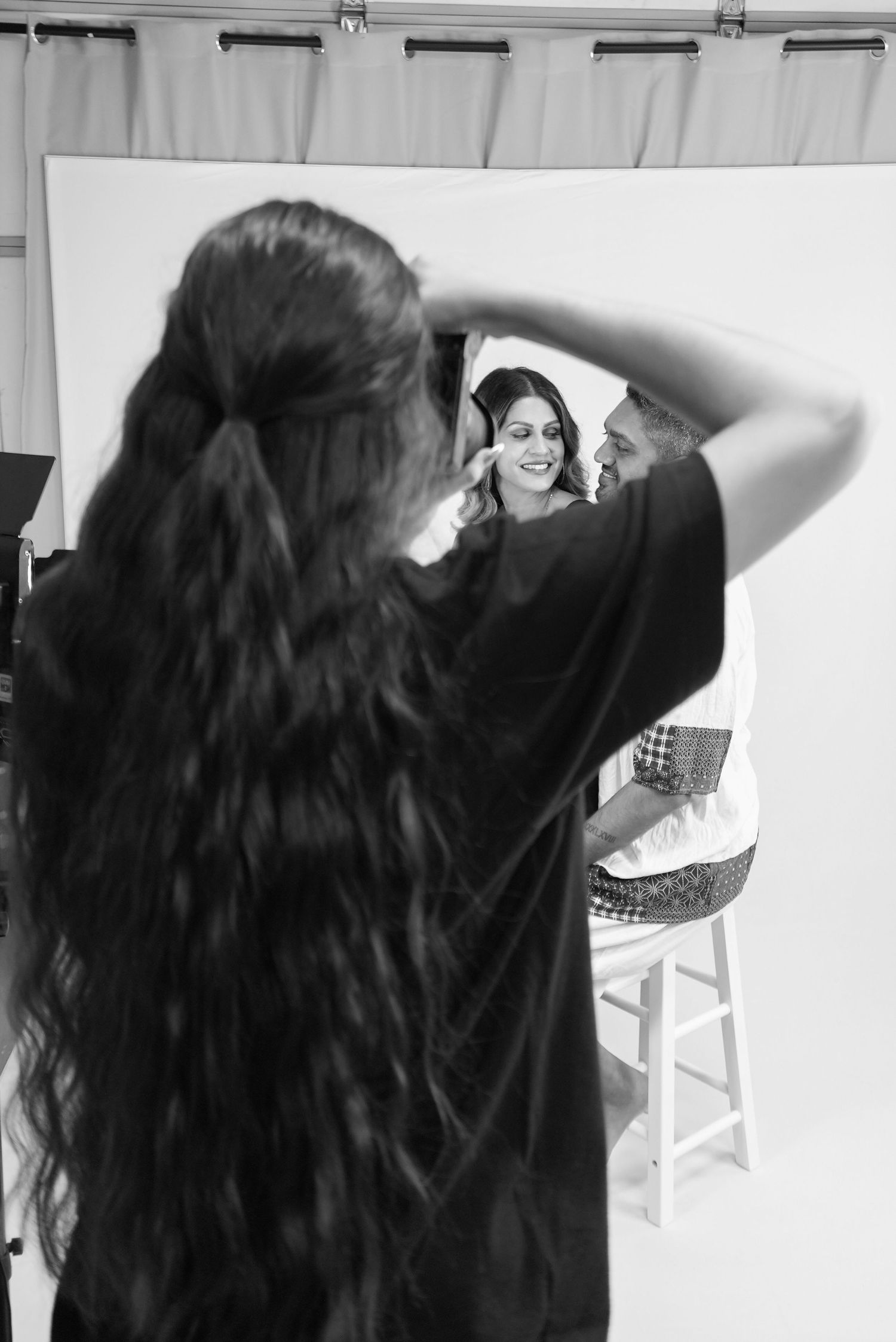 Black and white photo of a out-of-focus photographer (Ellie) capturing studio portraits of two in-focus smiling subjects.