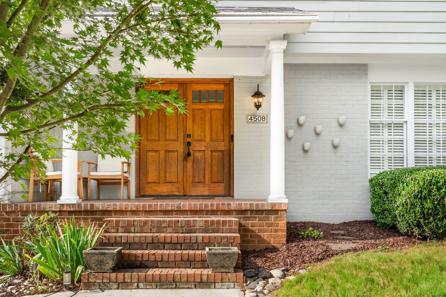 Charming home exterior showcasing strong curb appeal with brick steps, double wooden front doors, white columns, and landscaped greenery.