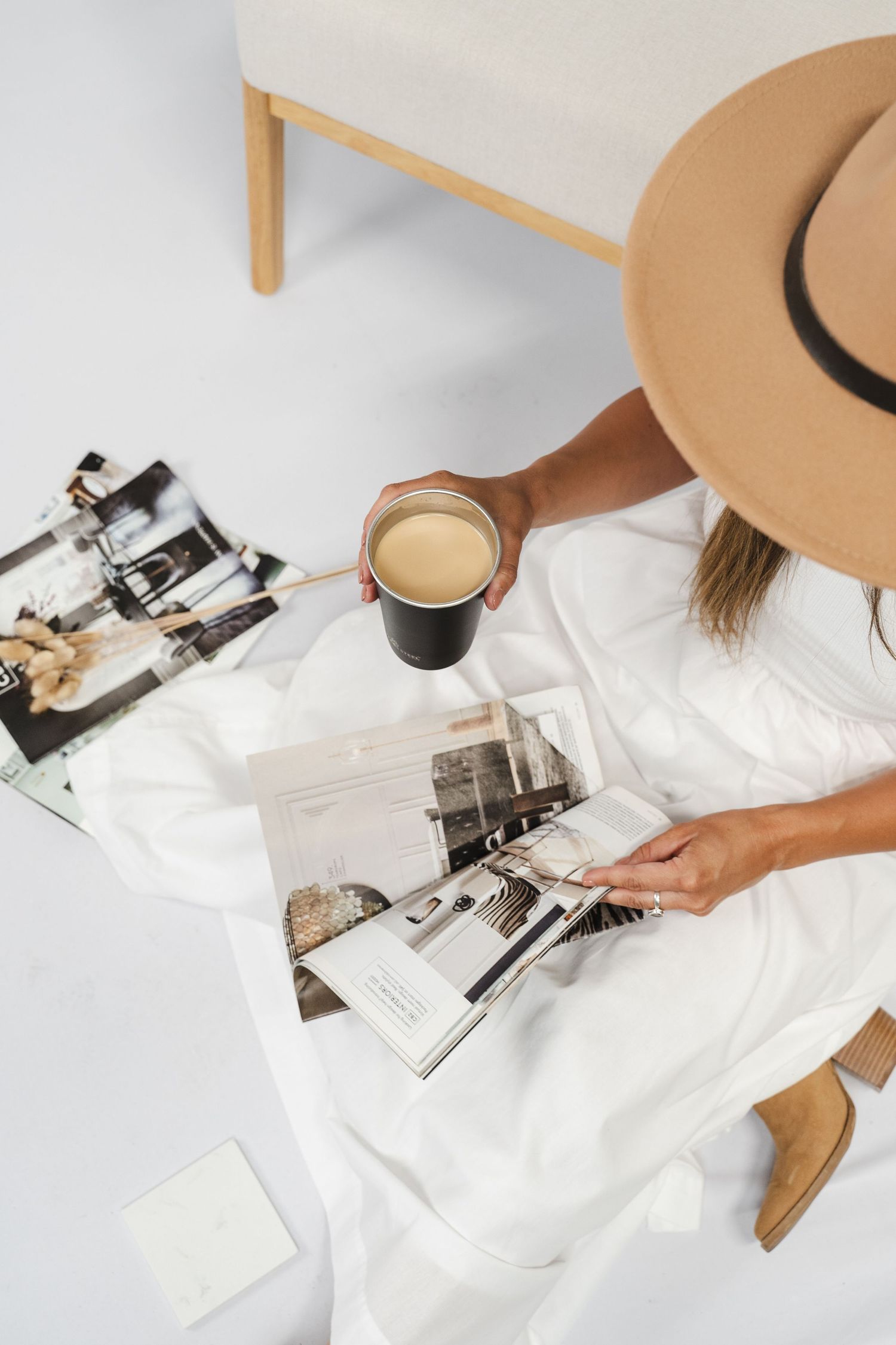 Flat lay, overhead lifestyle photo of a woman in a wide-brim hat reading magazines with coffee.