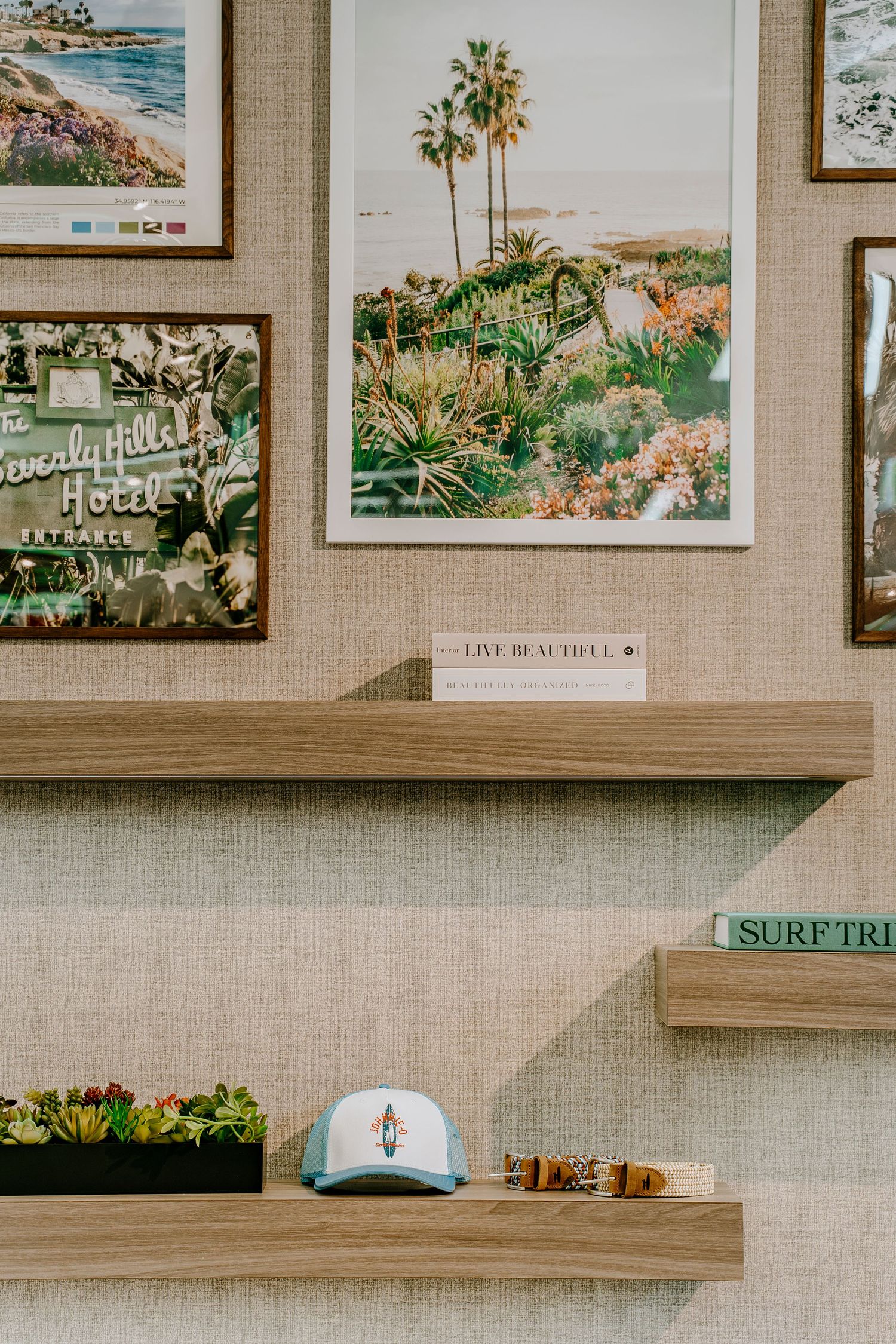 Interior wall display with framed coastal artwork, wood floating shelves, succulents, and quirky decorative accents.
