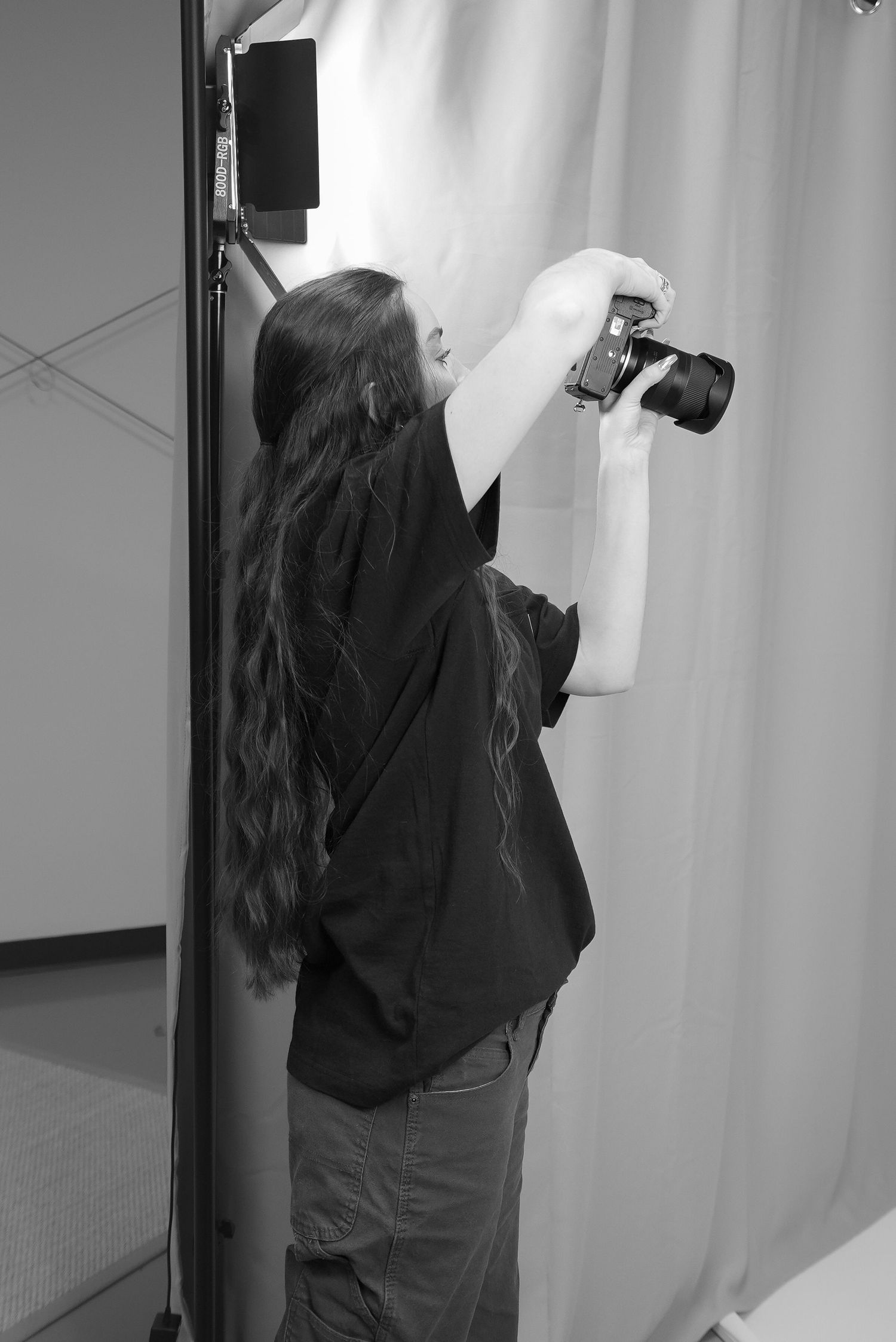 Black and white image of a professional photographer (Ellie) raising a camera to get an overhead shot in a professional studio setup.