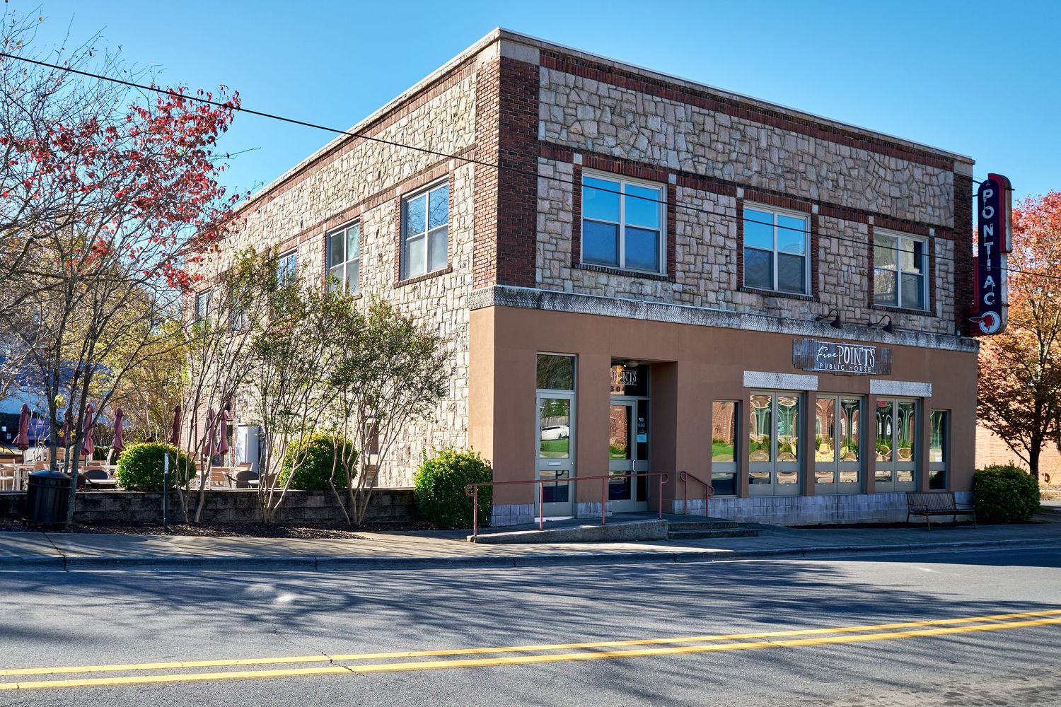 Two-story brick and stone commercial building with ground floor retail space and residential units above on a tree-lined street.