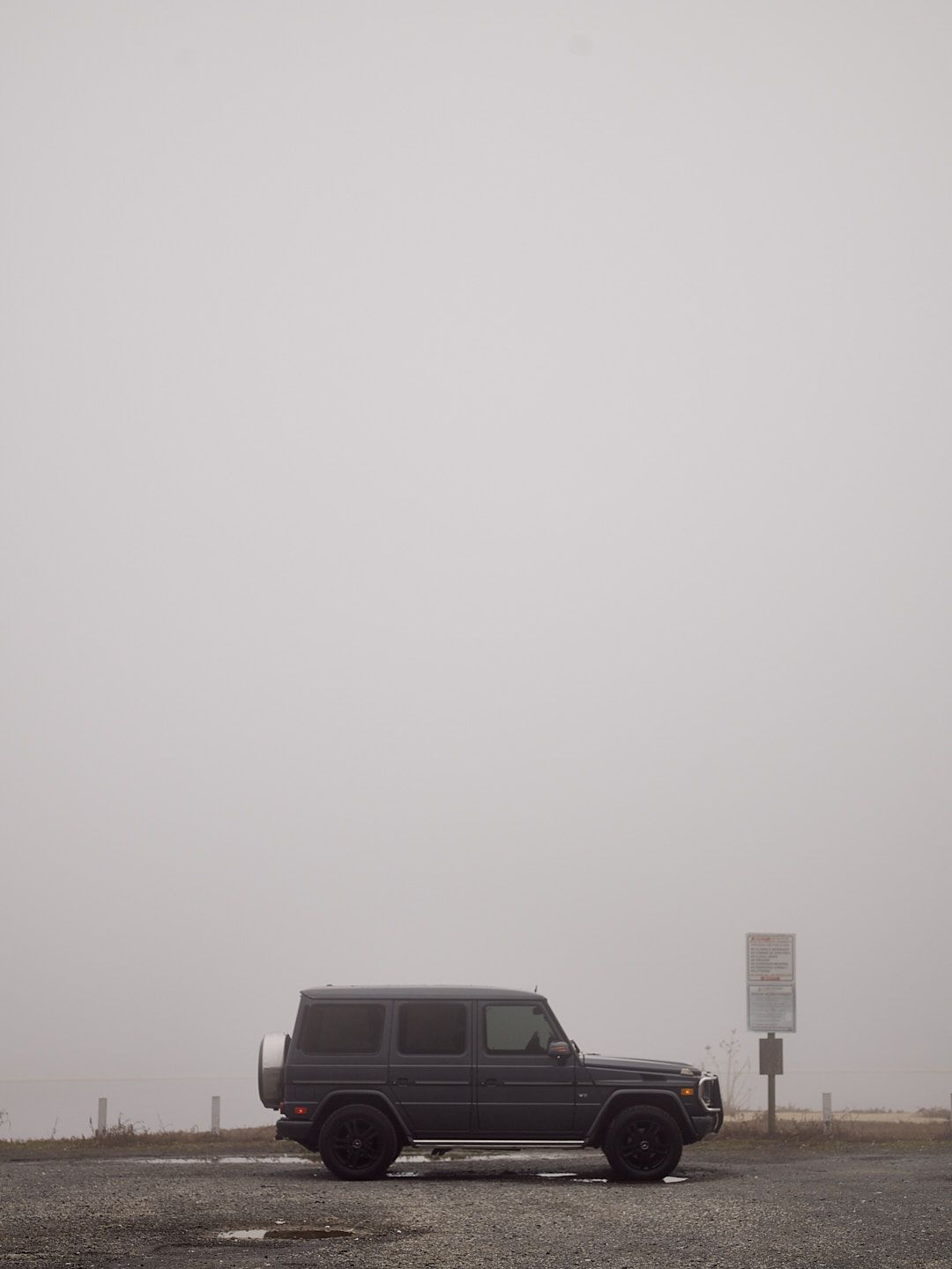 Three black SUVs parked in thick fog on a misty road create an atmospheric scene.
