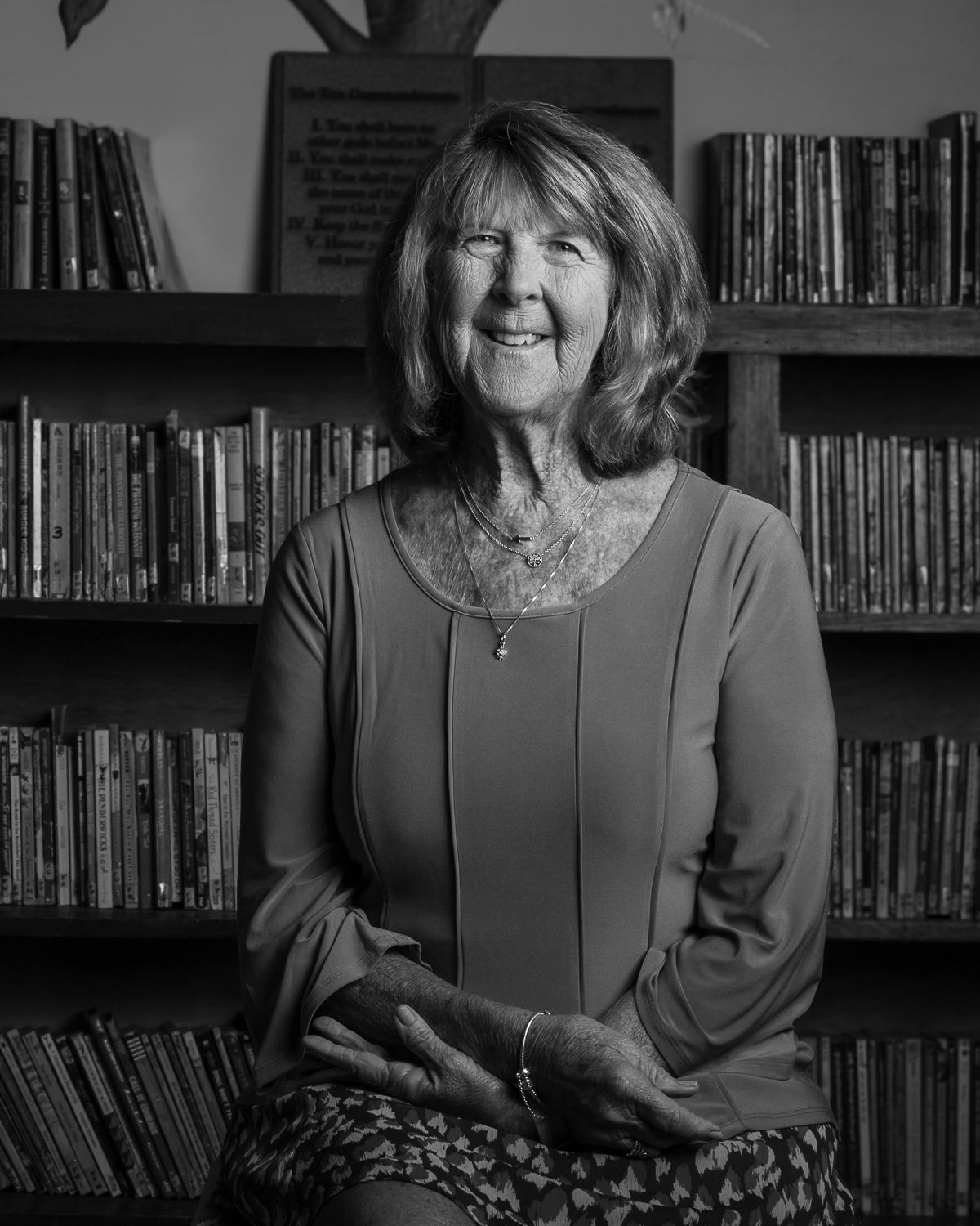 Black and white portrait in a library setting with bookshelves in background.