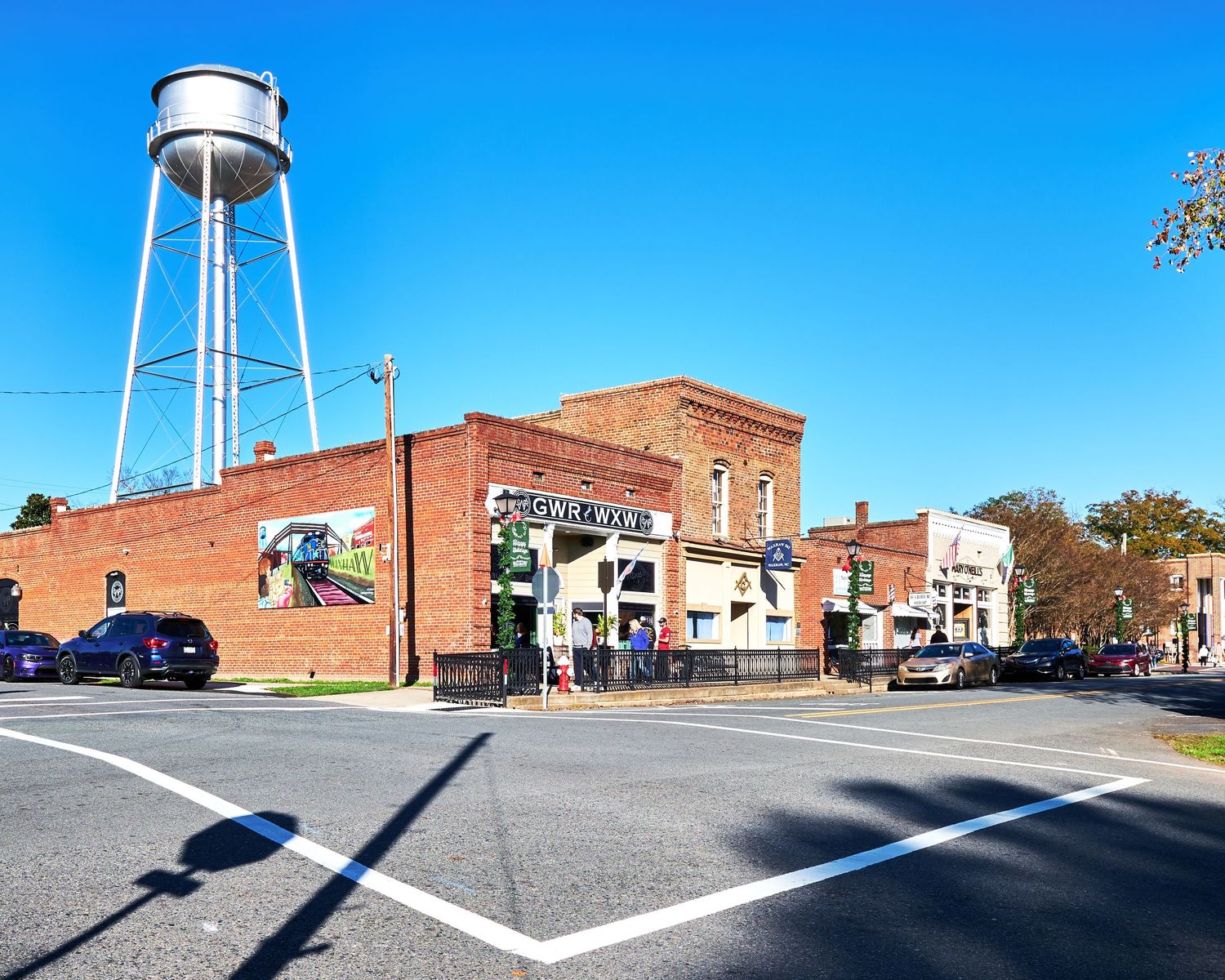 A panoramic view of a small town street with brick buildings and water towers against a bright blue sky.