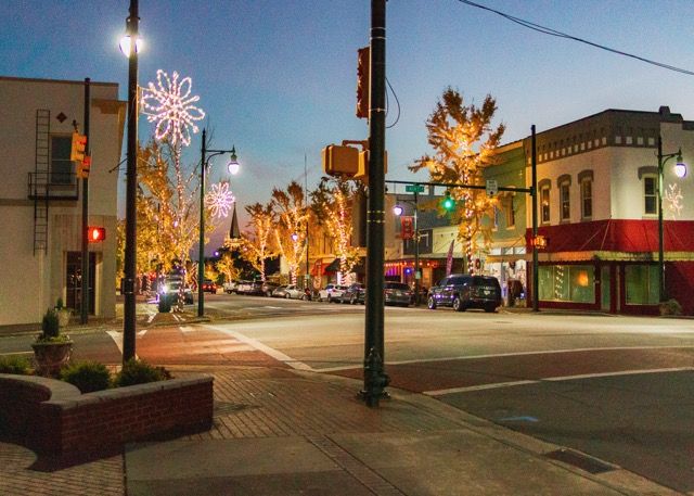 Illuminated holiday light displays line a small town street at dusk creating a festive winter atmosphere.