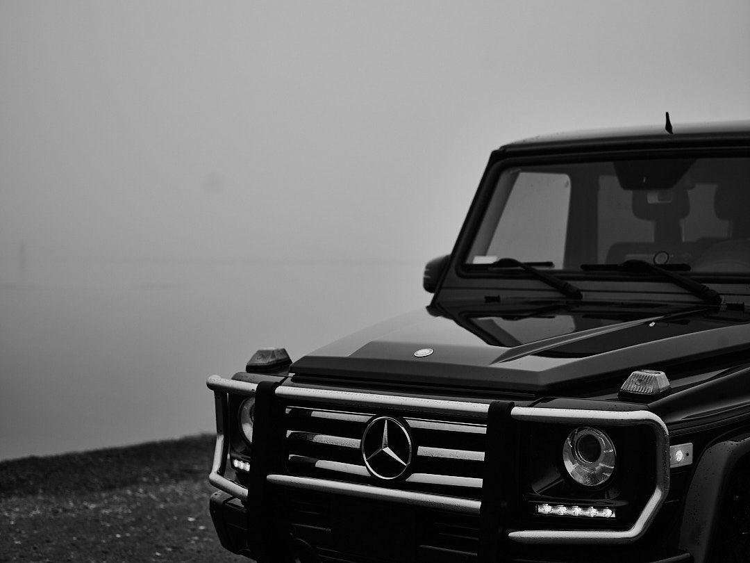 A sleek black Mercedes G-Wagon SUV with LED headlights parked against a dark background.