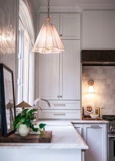 A modern white kitchen with pendant lighting features elegant crown molding, marble countertops, and sleek cabinetry.