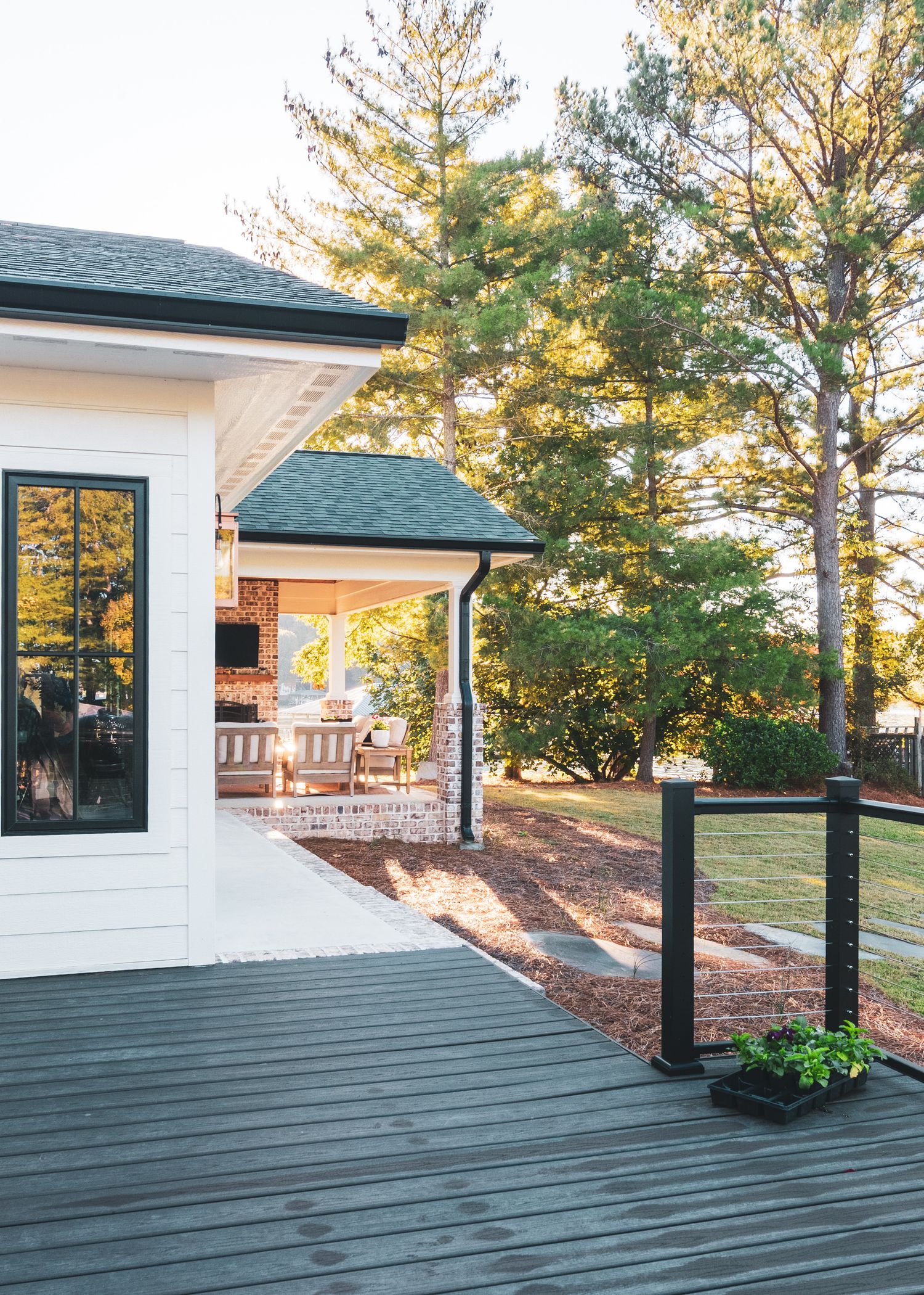 Modern deck with dark gray flooring and white railings surrounded by tall pine trees in a backyard setting.