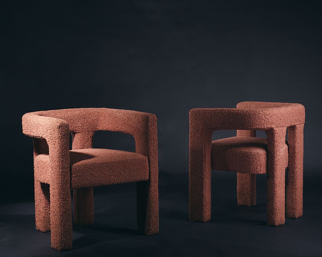Two retro-style curved armchairs in dusty rose bouclé fabric with chunky geometric frames against dark background.