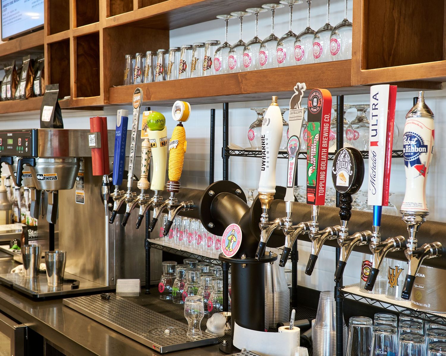Long bar counter with multiple beer taps and hanging glassware in a rustic wooden setting.