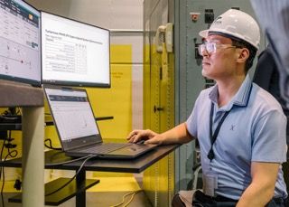 Industrial workers review technical specifications and data on computer monitors in a manufacturing facility.