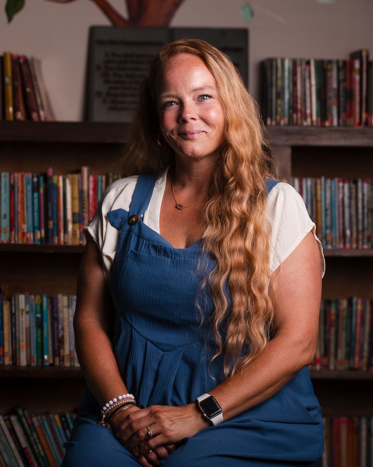Professional Headshots in a library setting with rows of books visible on shelves in warm lighting.