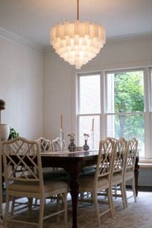 A modern dining room features a white capiz shell chandelier and elegant wooden chairs arranged around a dark table.