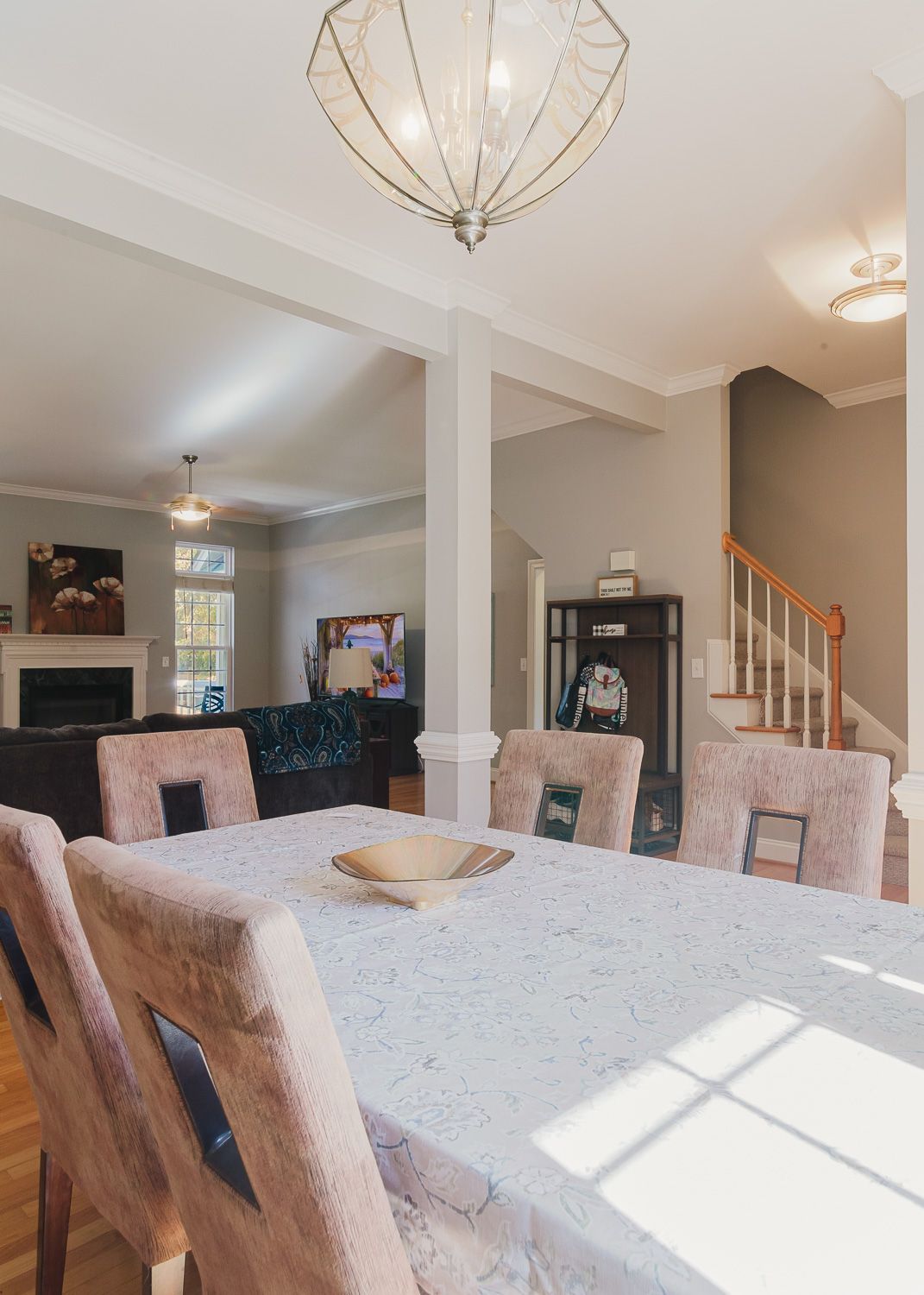Modern dining room with marble table, plush chairs, geometric pendant light, and view of staircase in open floor plan interior.