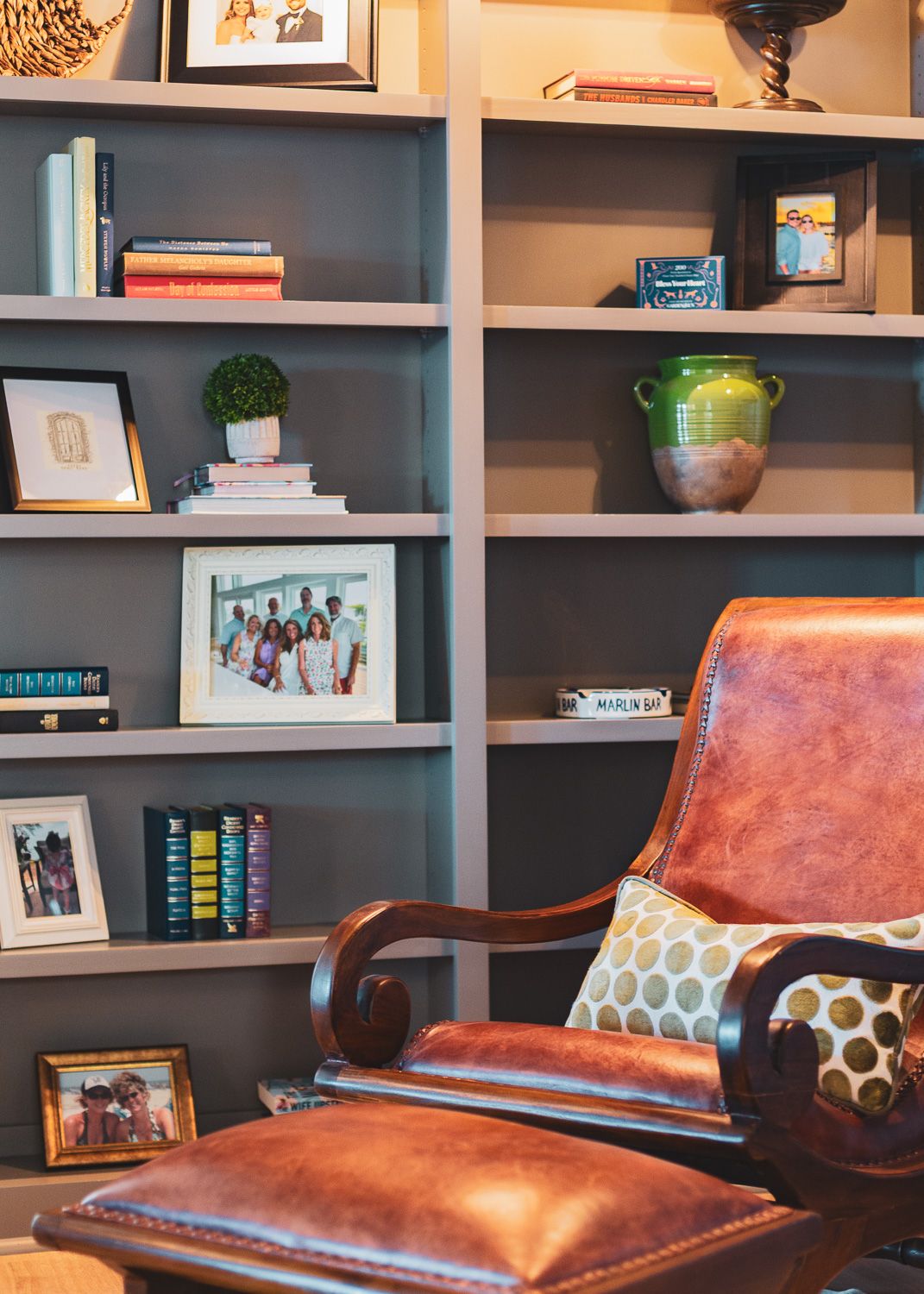 Built-in bookshelves with dark blue backing feature leather chairs and decorative accessories in a cozy reading nook.