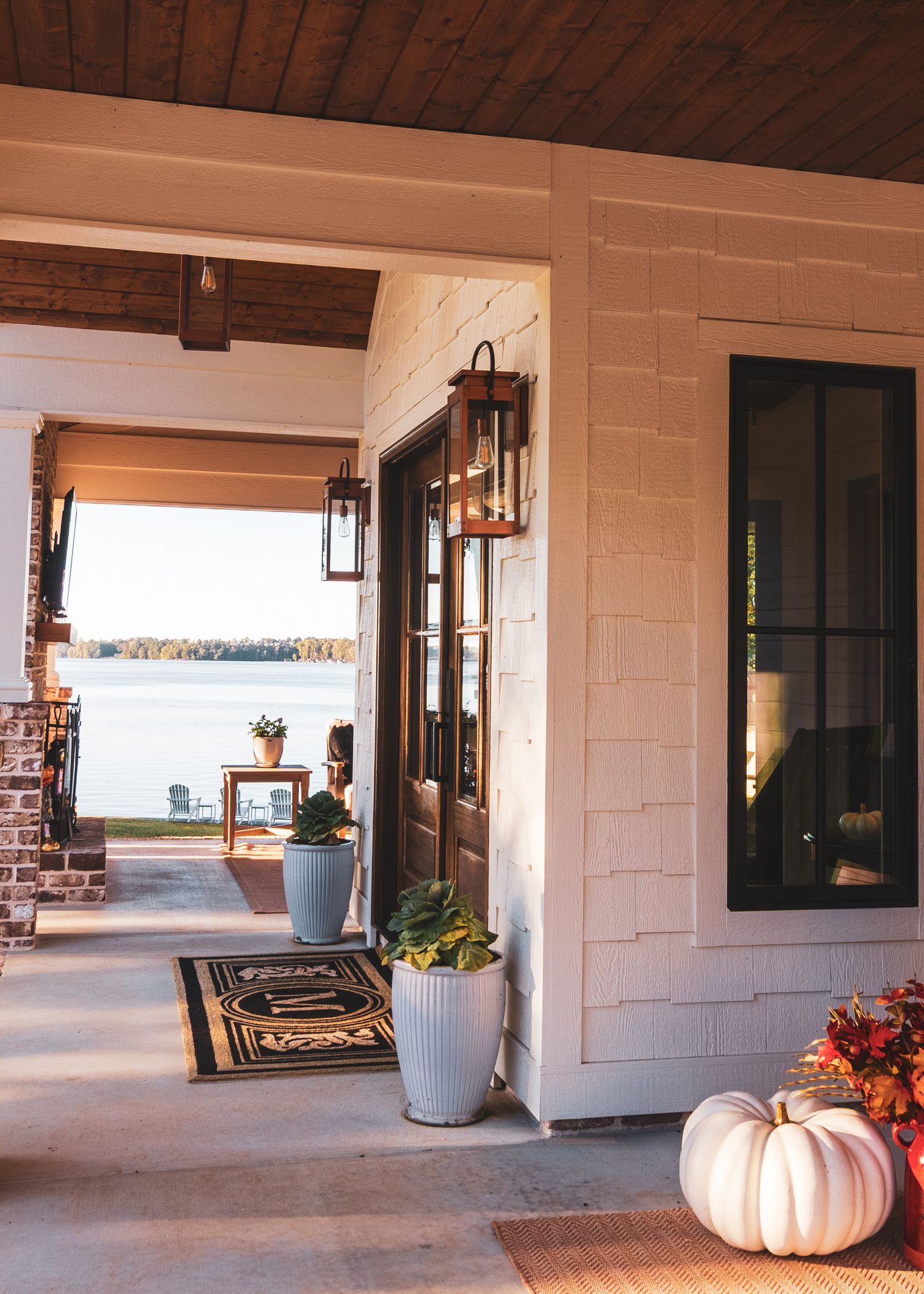 A covered walkway with white walls and brick accents features decorative pumpkins and planters along the entrance.