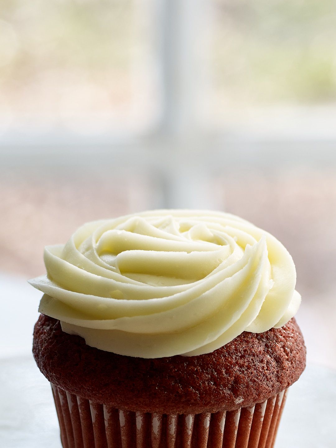 Red velvet cupcakes with swirled cream cheese frosting arranged in a row on a white surface.