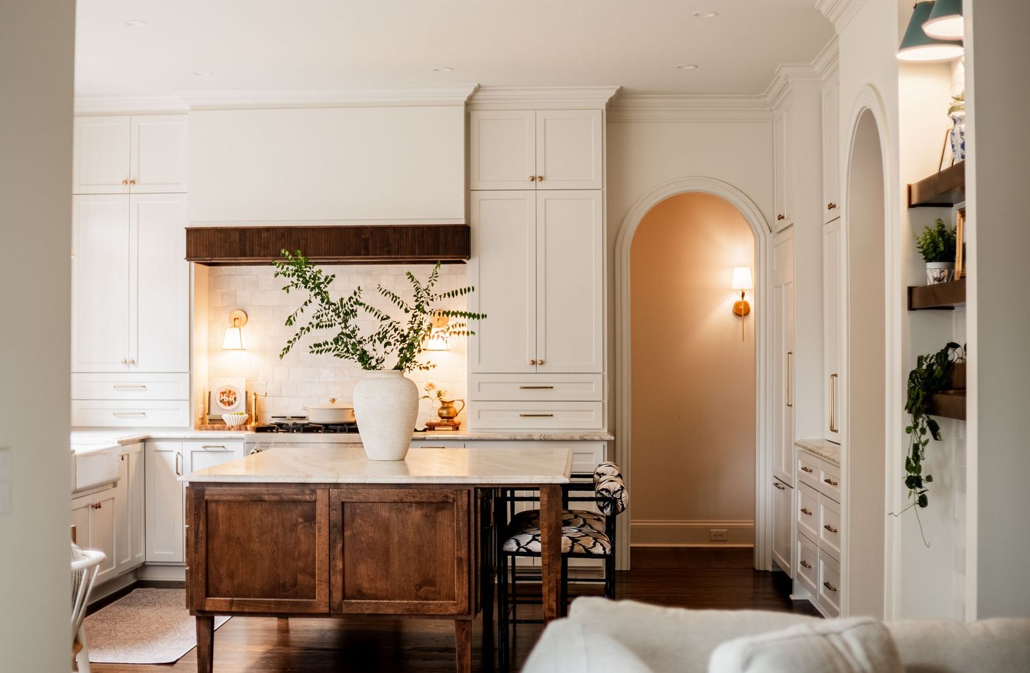Elegant white kitchen interior with wooden accents and arched doorways creating a bright, spacious atmosphere.