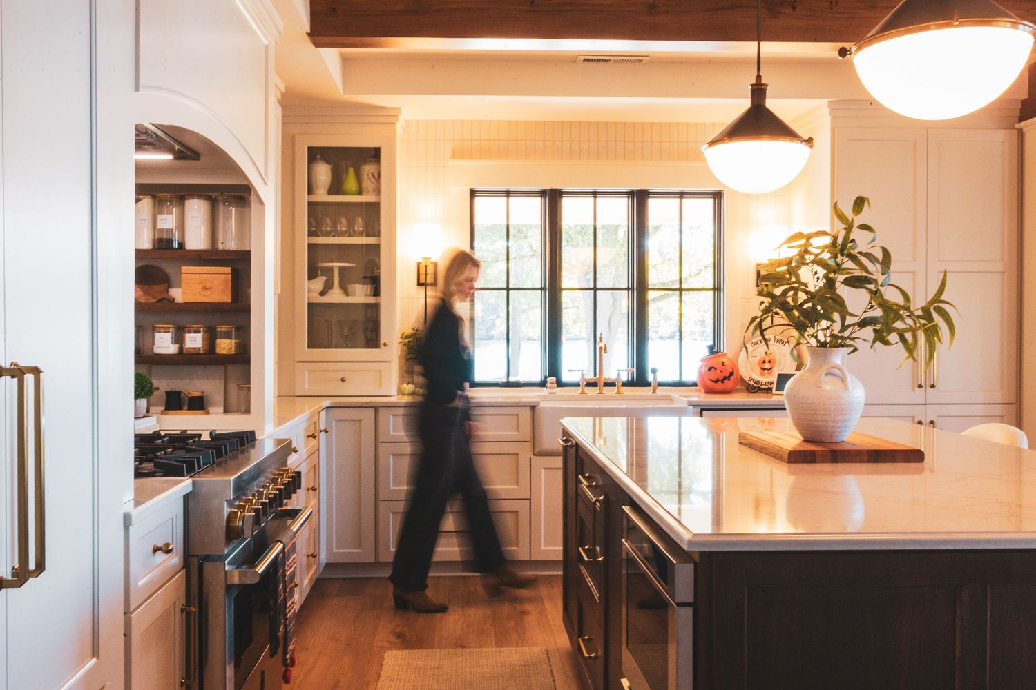 Modern white kitchen with pendant lighting, wood floors, and open shelving features clean lines and natural light.