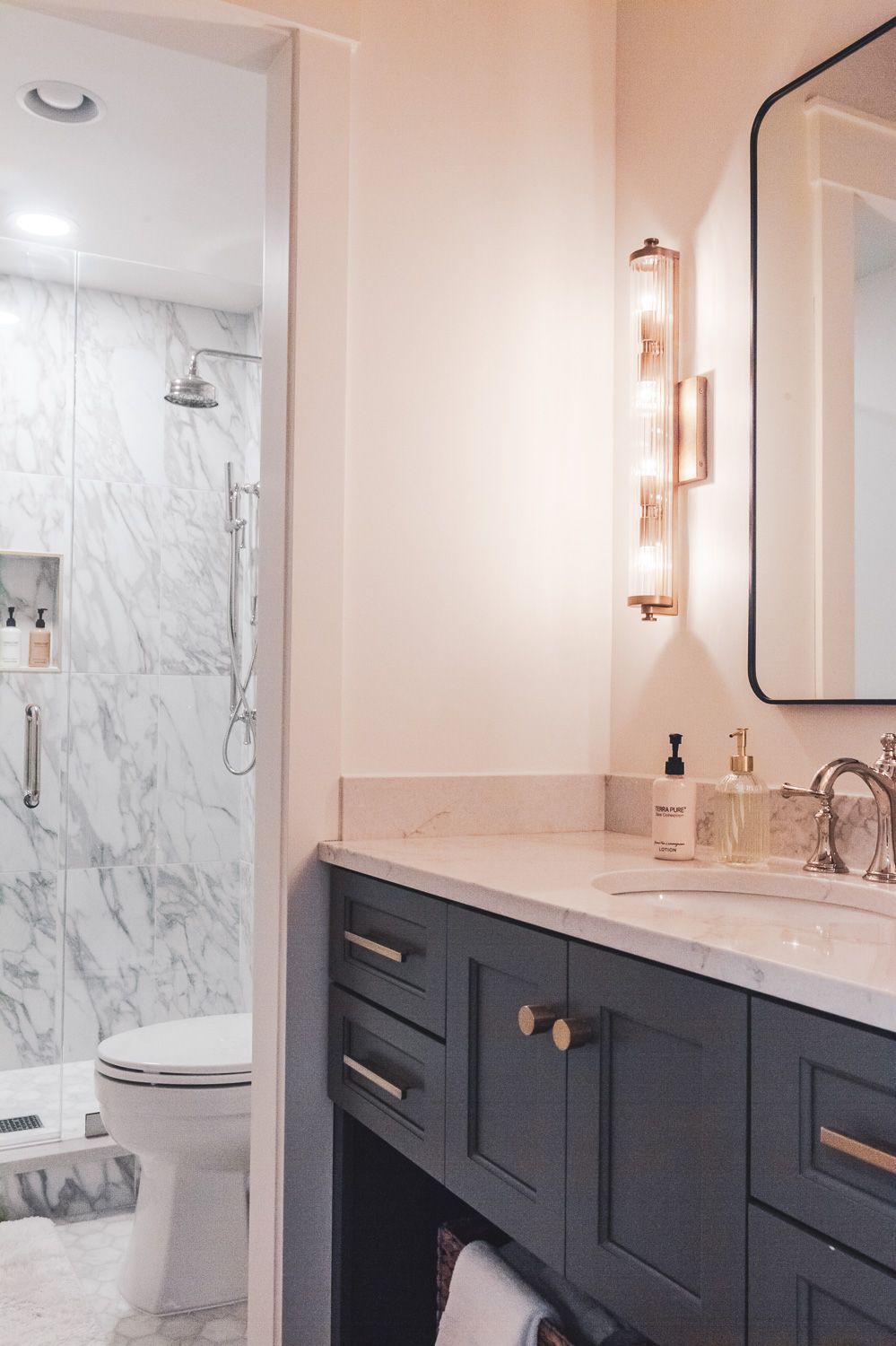 Modern bathroom interior with dark navy vanity cabinets, marble walls, and copper hardware accents.