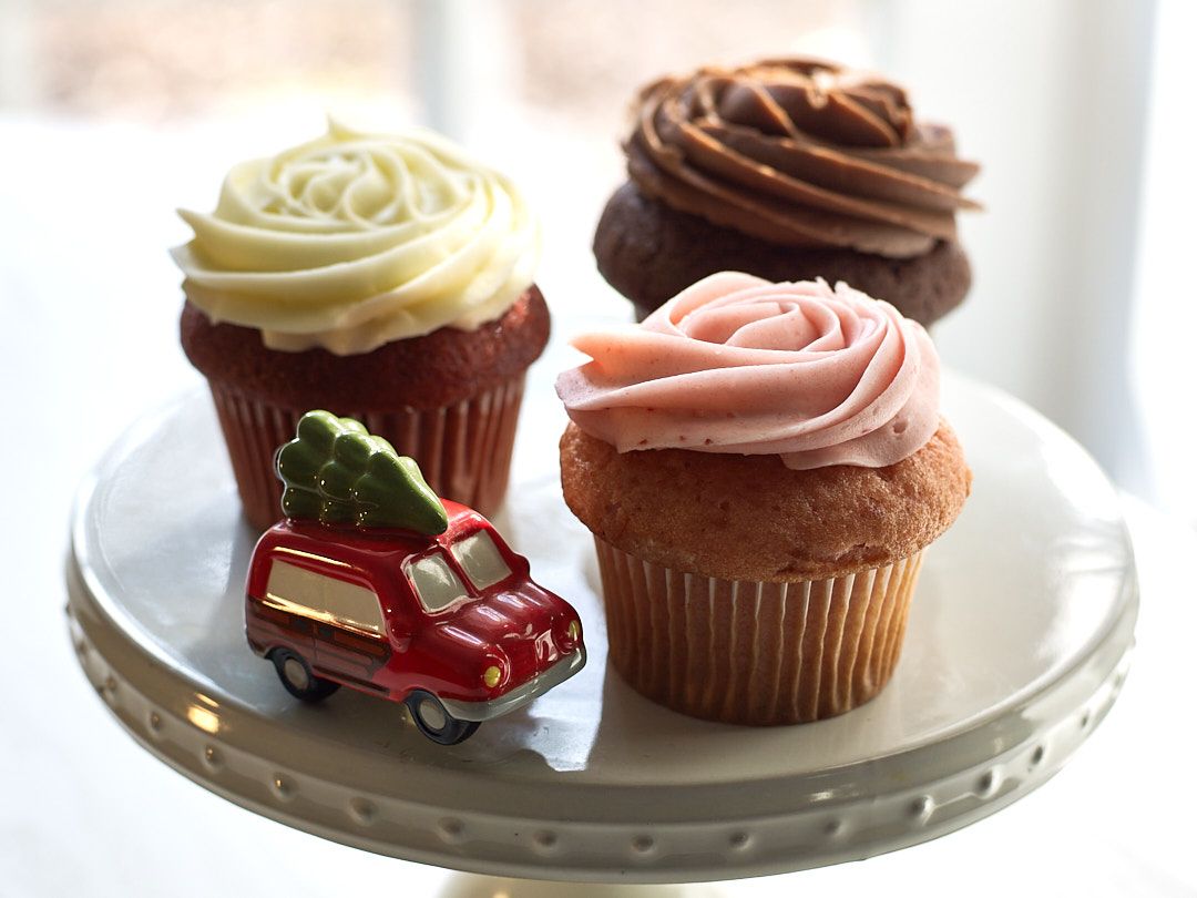 Assorted gourmet cupcakes with colorful frosting displayed on white ceramic plates.