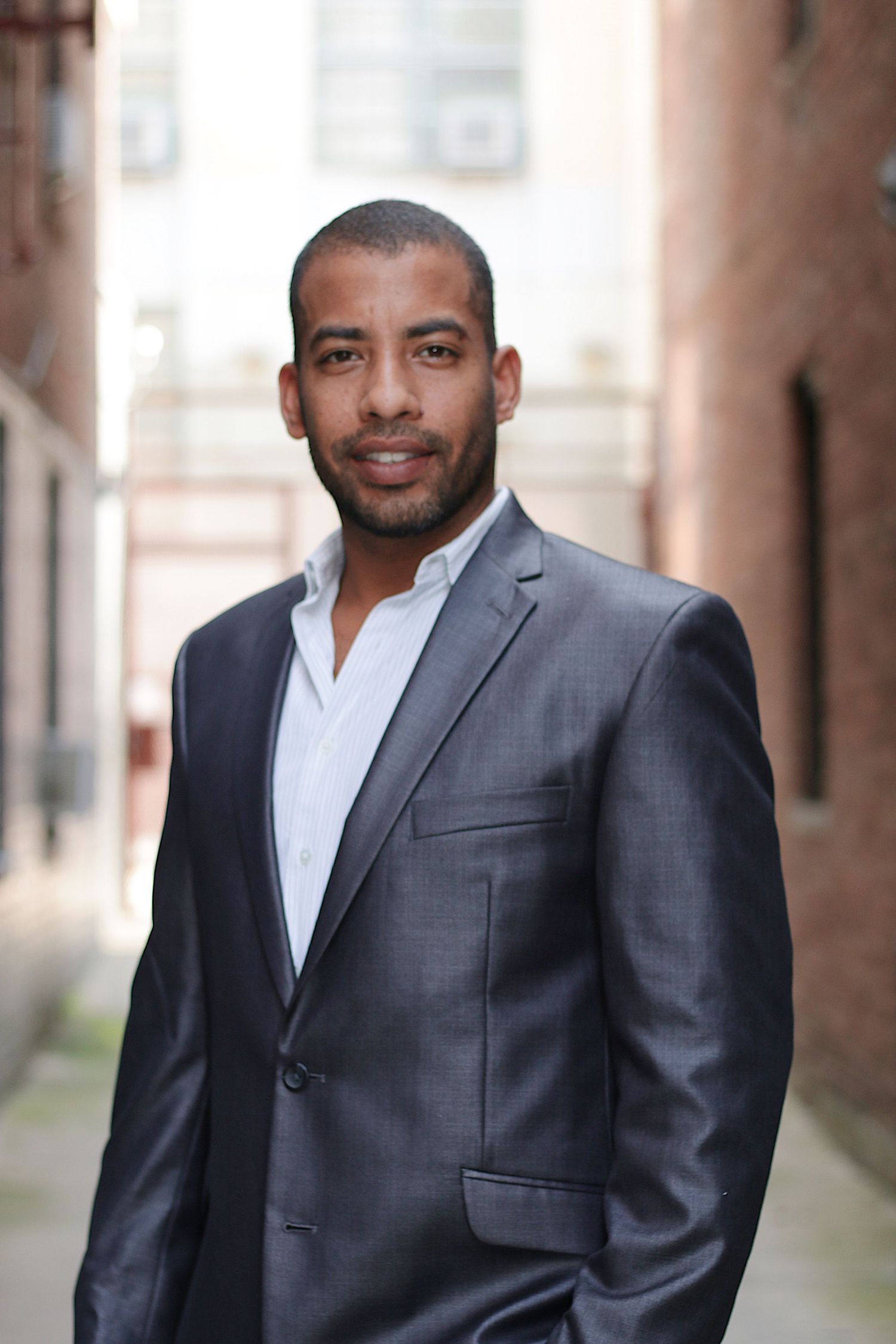 Professional headshot of a person wearing a grey suit jacket and white dress shirt against a blurred background.
