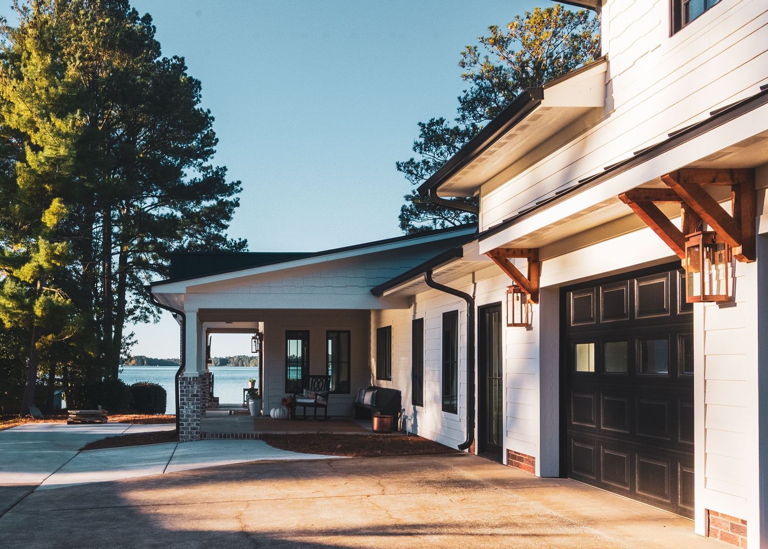 Modern coastal home exterior with white walls, dark doors, wooden beams and covered walkway leading to water view.