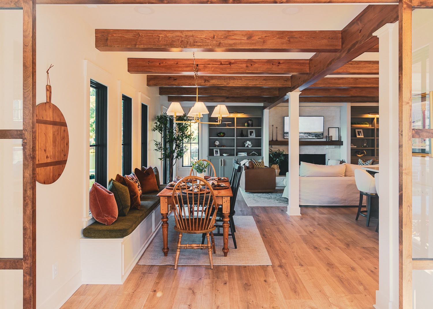 Modern open concept interior with wooden floors and exposed beams features sleek white columns and natural lighting.