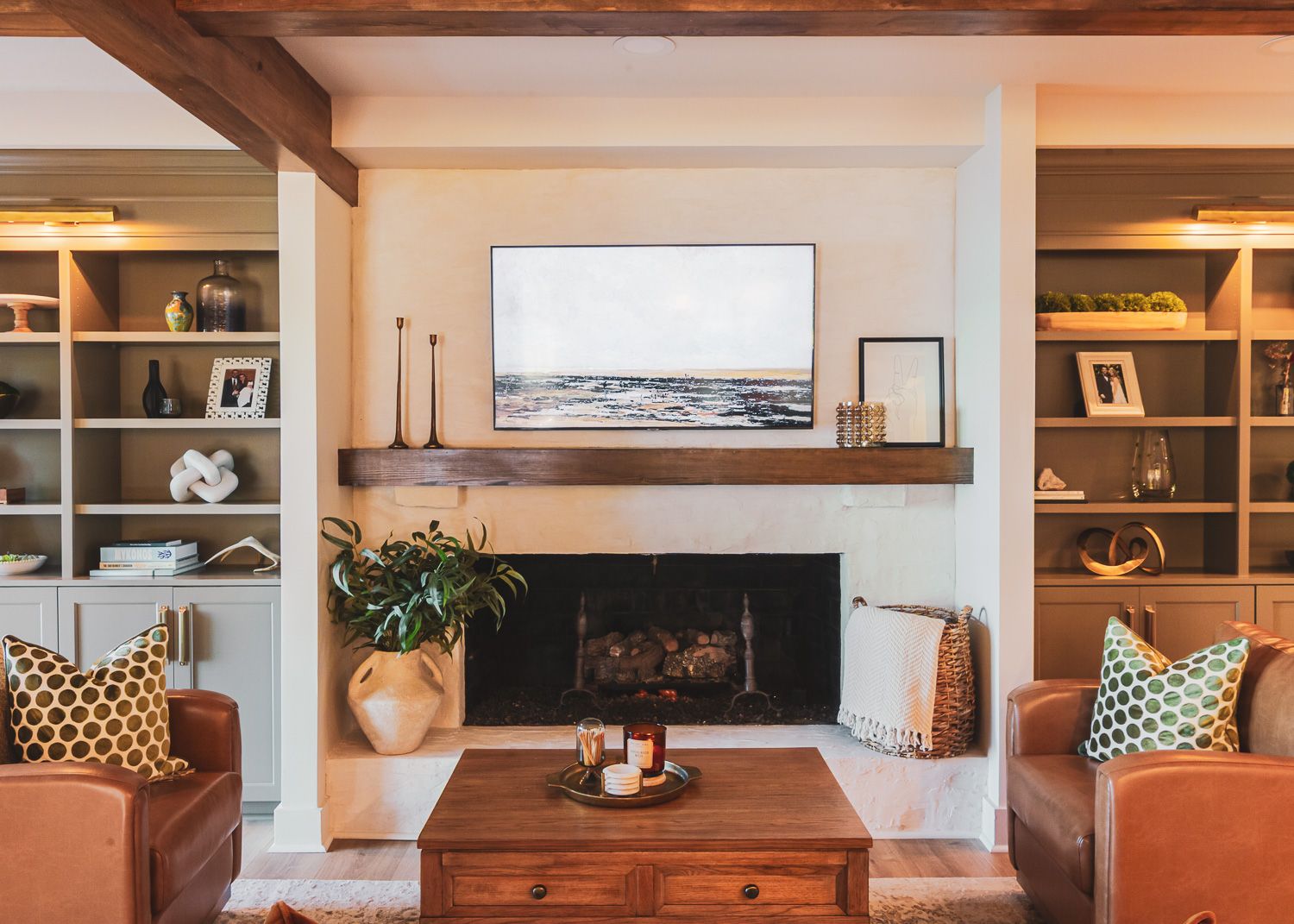 Coastal-style living room interior with built-in shelving, wooden beams, and decorative pillows on white furniture.