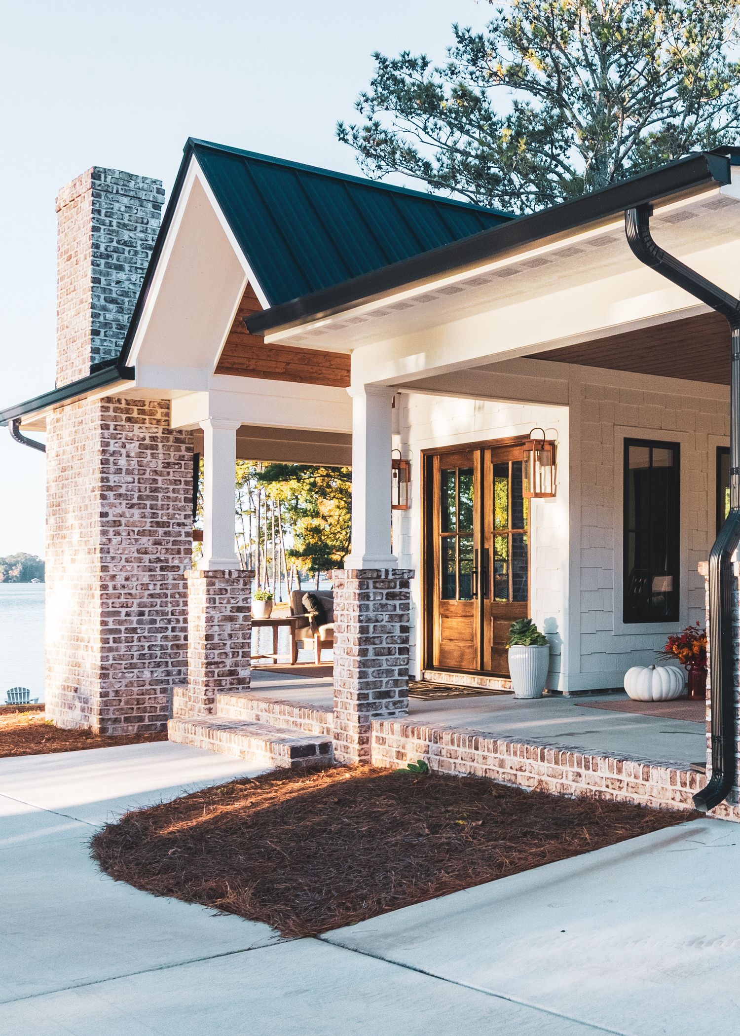 Modern farmhouse entrance with brick columns, wooden door, and covered porch featuring dark blue roof and white trim details.