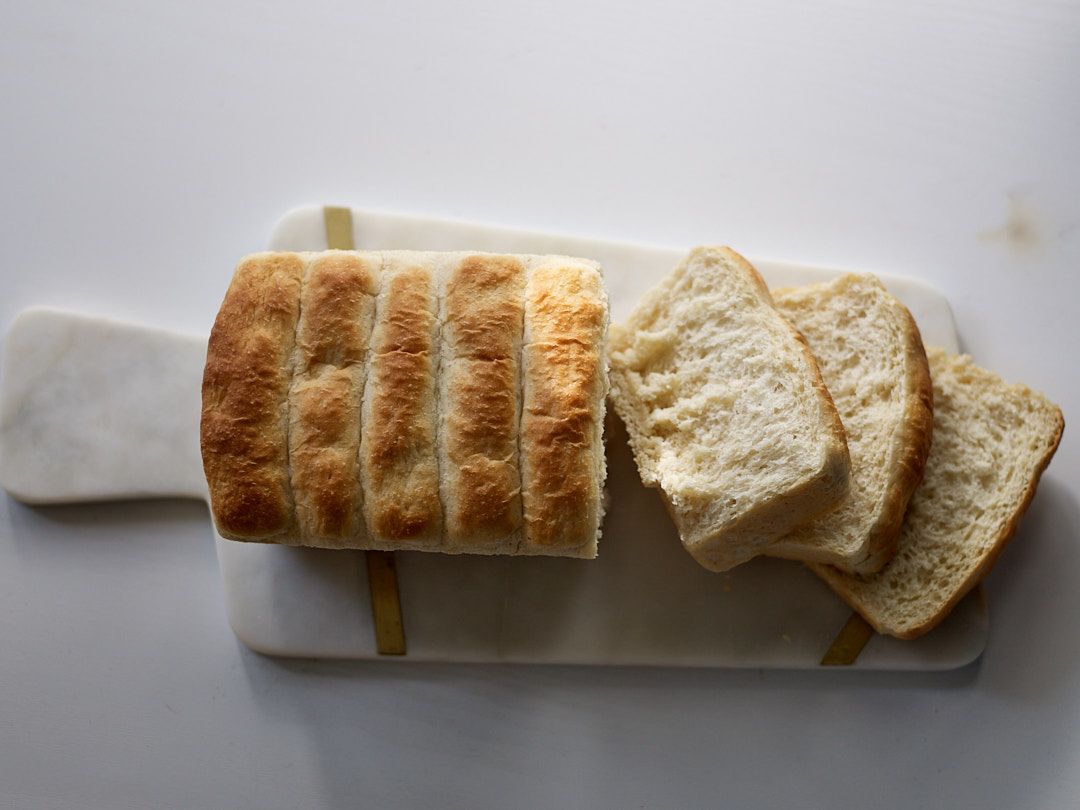 Sliced white sandwich bread arranged on a marble cutting board with natural lighting from above.