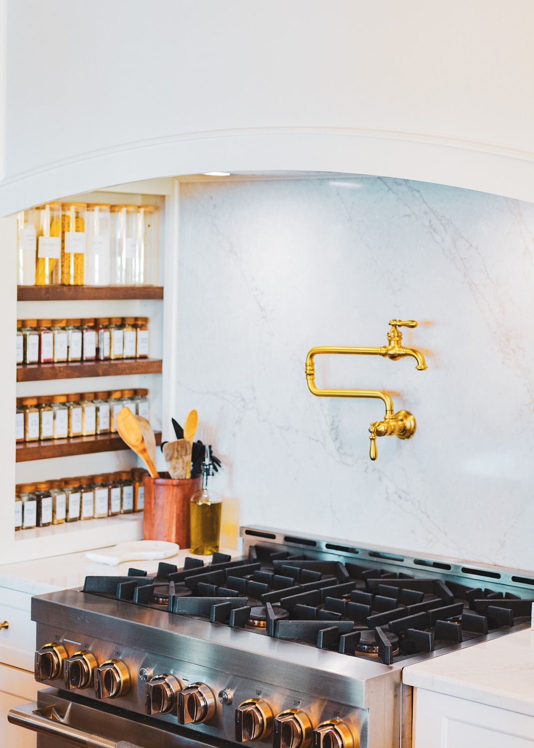 Modern kitchen features gold faucet fixtures mounted above black stovetop with white cabinets and open shelving.