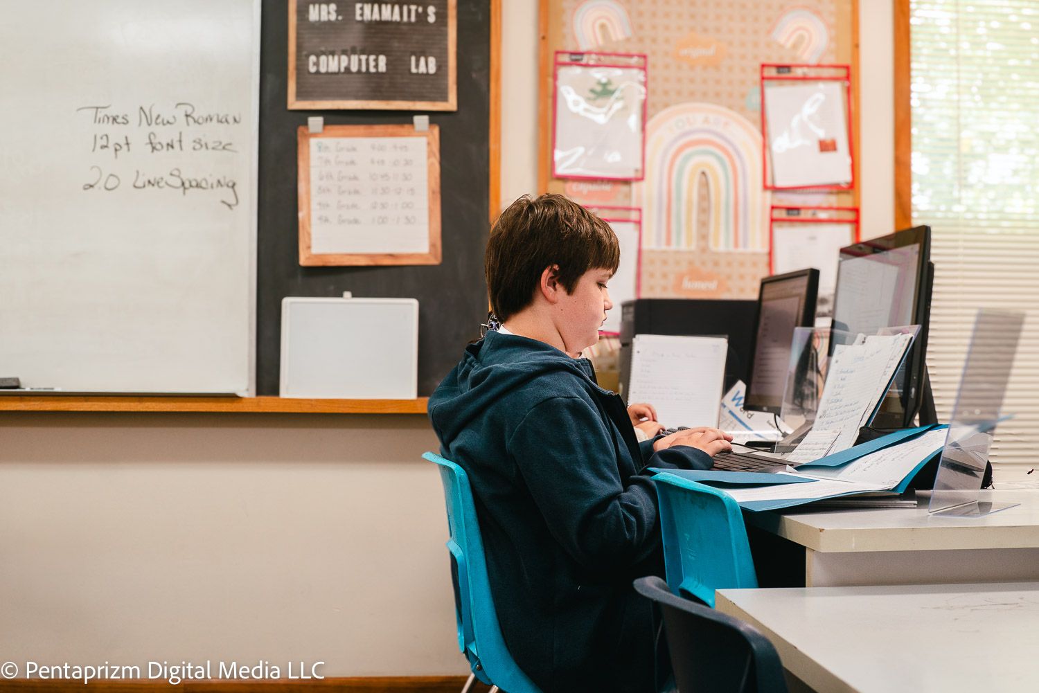 Students work at computer stations in a classroom with educational posters on the walls.