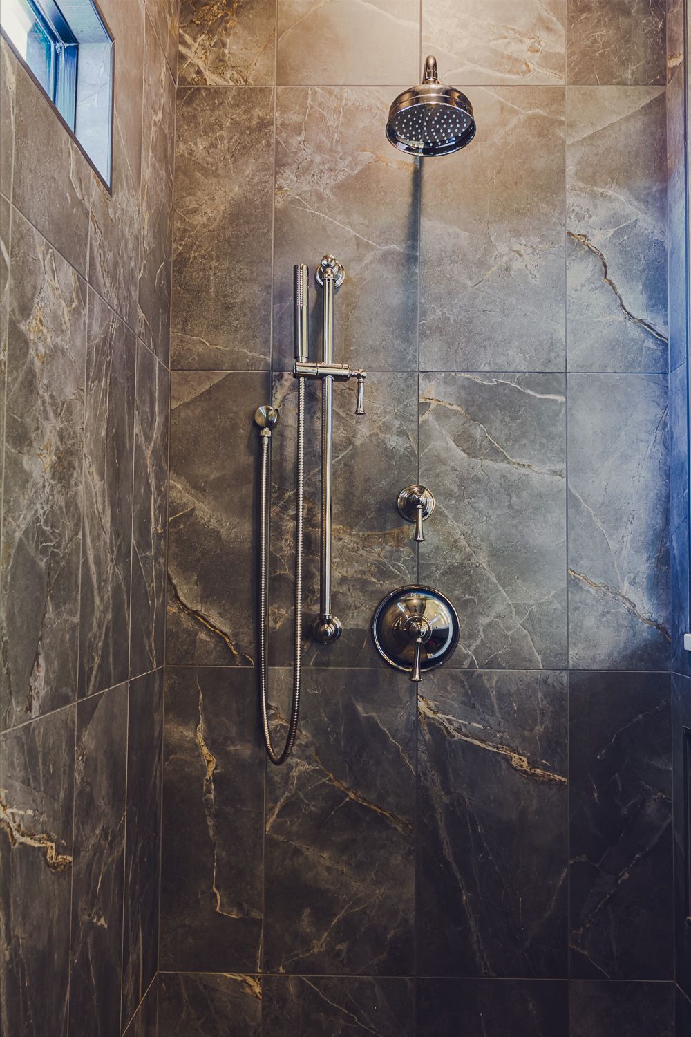 Modern bathroom shower with dark marble tile walls and chrome fixtures featuring multiple showerheads and nozzles.