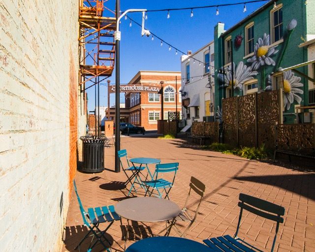 A cozy outdoor patio space with turquoise chairs and string lights between brick buildings in an urban setting.