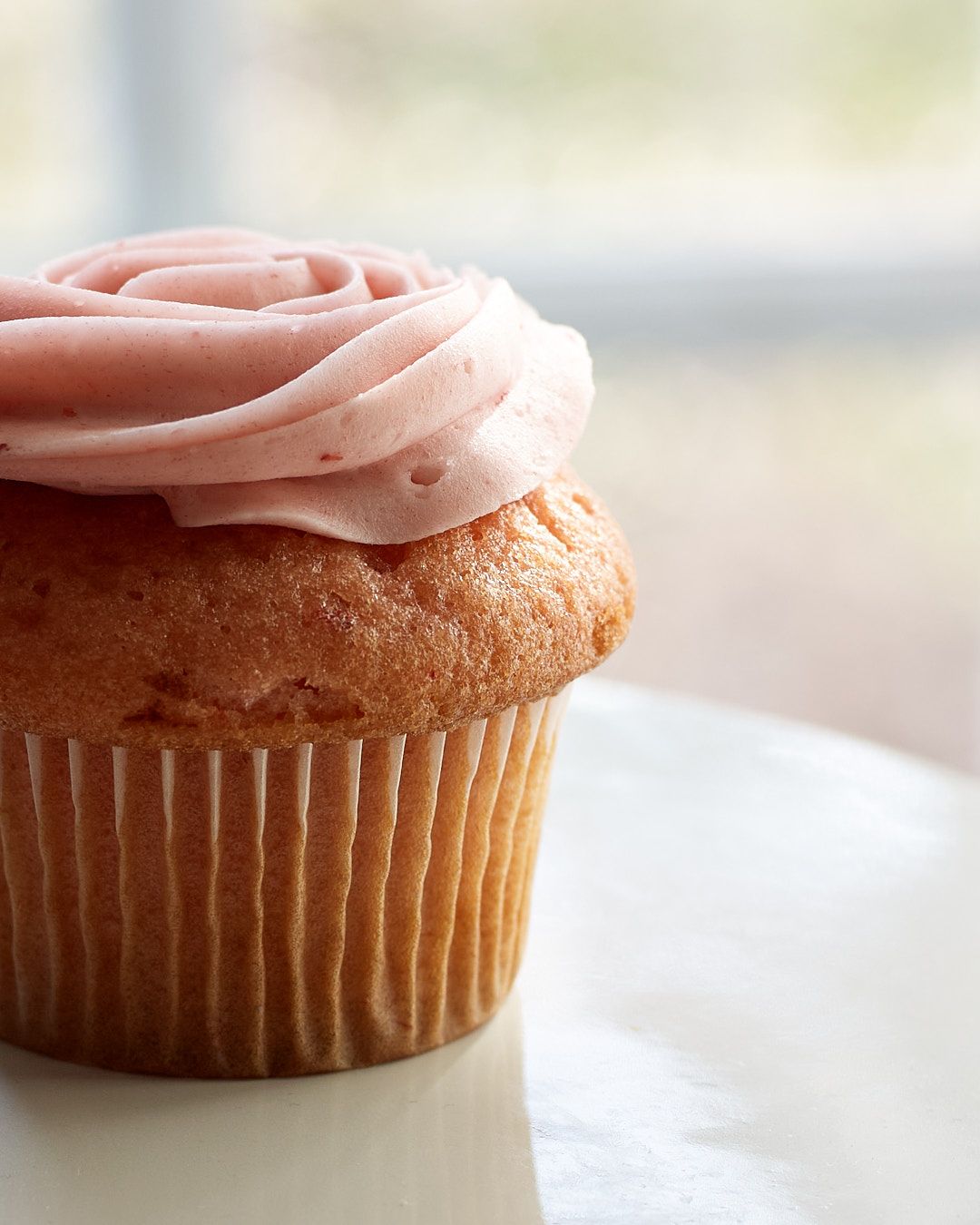 A close-up sequence showing a pink-frosted vanilla cupcake from different angles on a white surface.