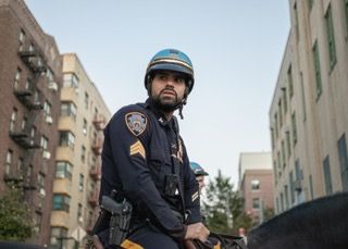 NYPD officers patrol on bicycles through an urban neighborhood with apartment buildings in the background.