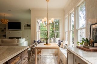Bright and airy panoramic view of a modern white kitchen with gold pendant lights and large windows overlooking greenery.