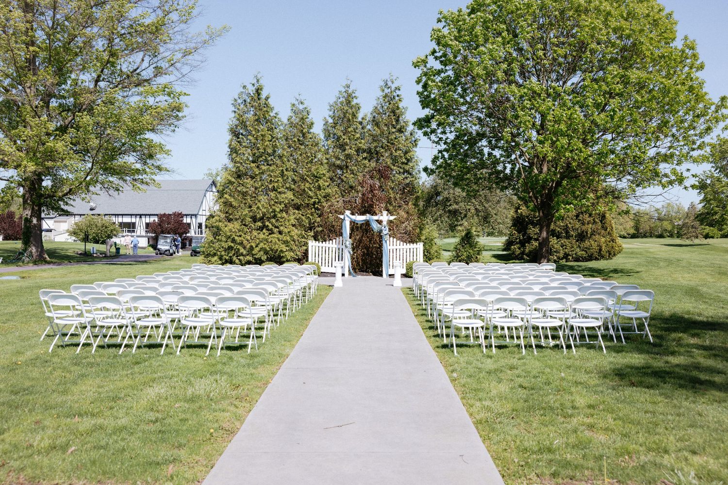 White chairs arranged in rows for an outdoor wedding ceremony on a sunny grassy lawn.