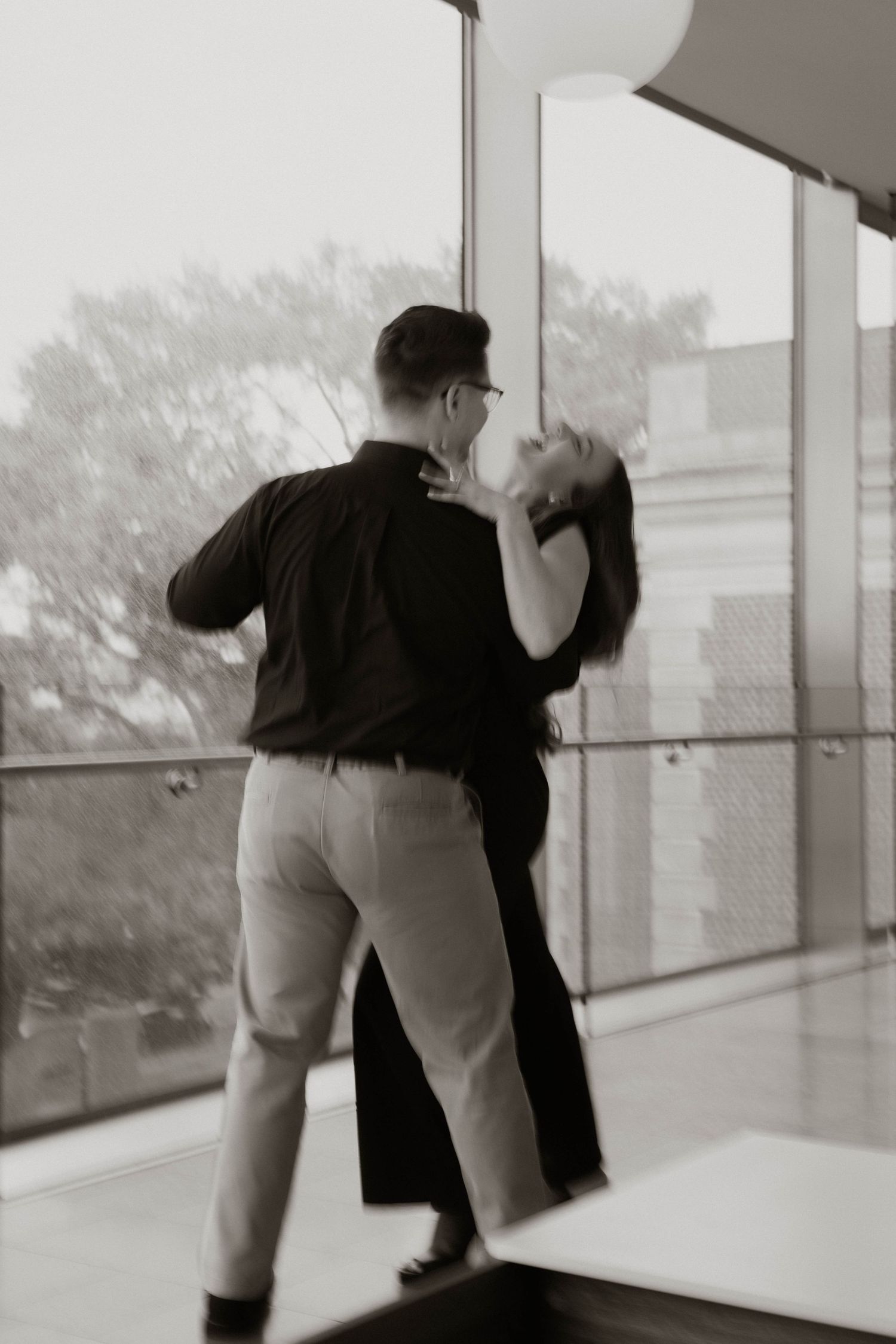 A romantic couple dancing together in black and white, captured in an elegant dip pose by a window.