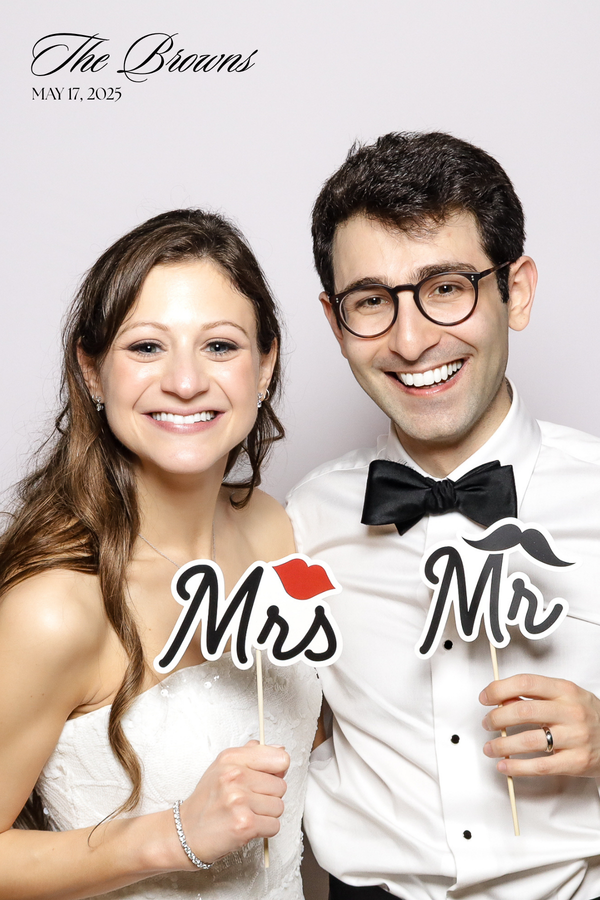 A wedding photo booth shot of a couple holding Mr and Mrs props while dressed in formal attire.