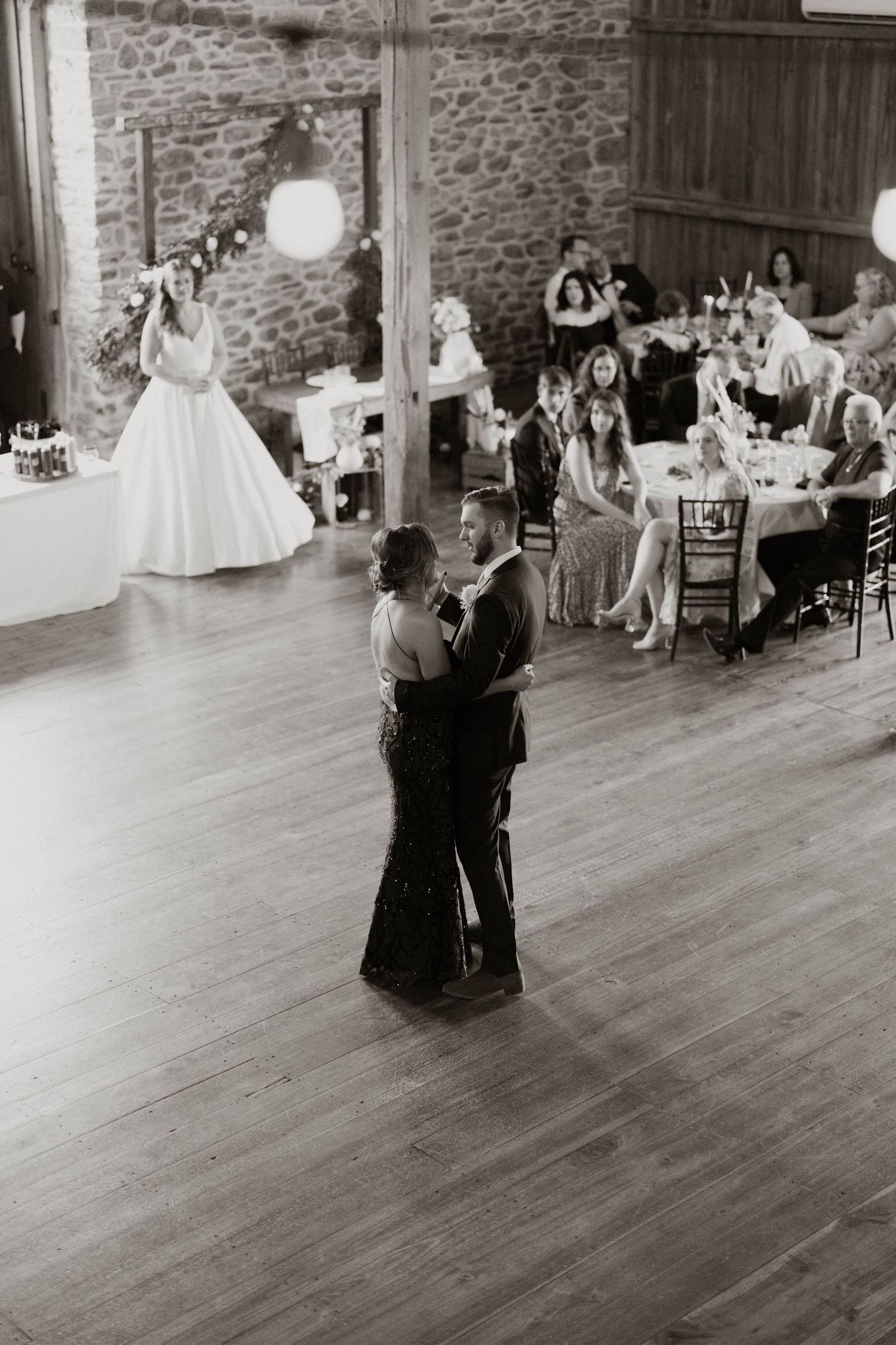 Couples dancing on a wooden floor during a wedding reception in a stone-walled venue.